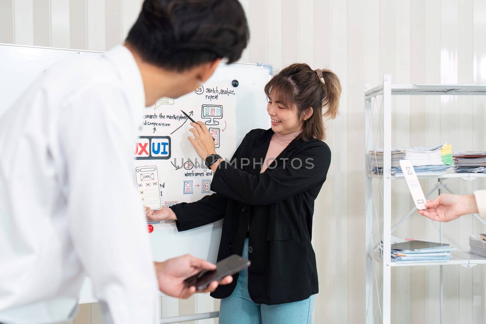 A vibrant workplace where a designer illustrates ideas on a whiteboard, contributing to UI UX planning through dynamic interaction with her team.