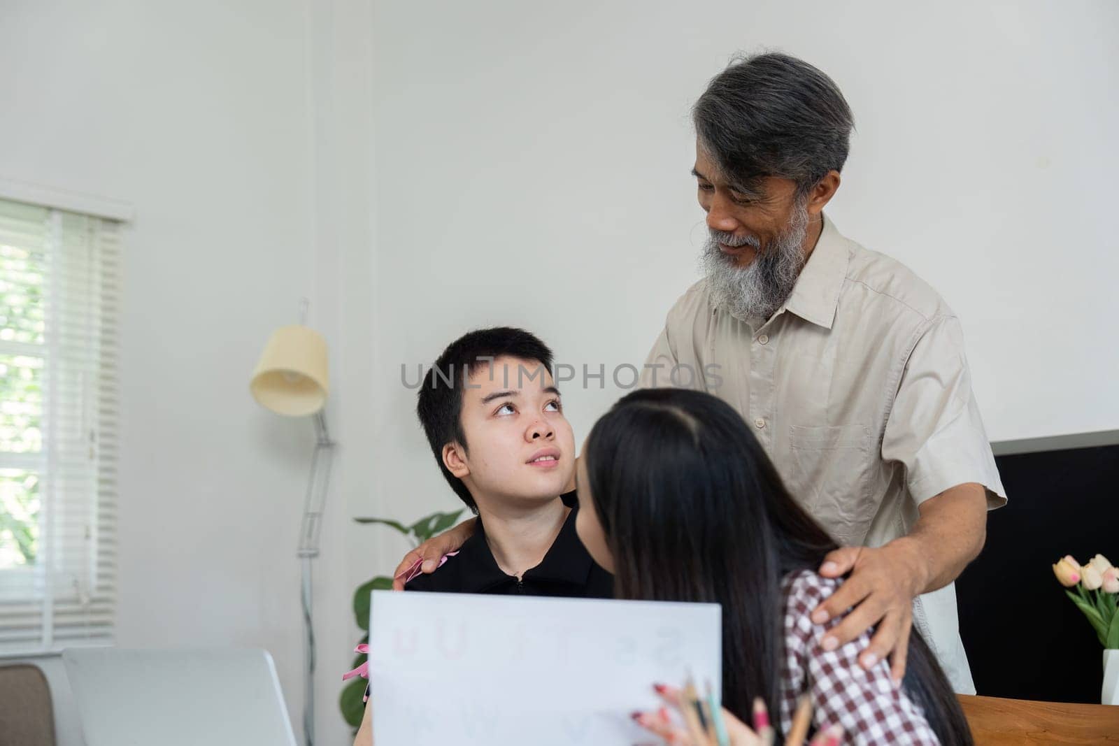 A grandfather shares a warm moment with his grandchildren, including a girl with Down syndrome, as they engage in learning together at home.