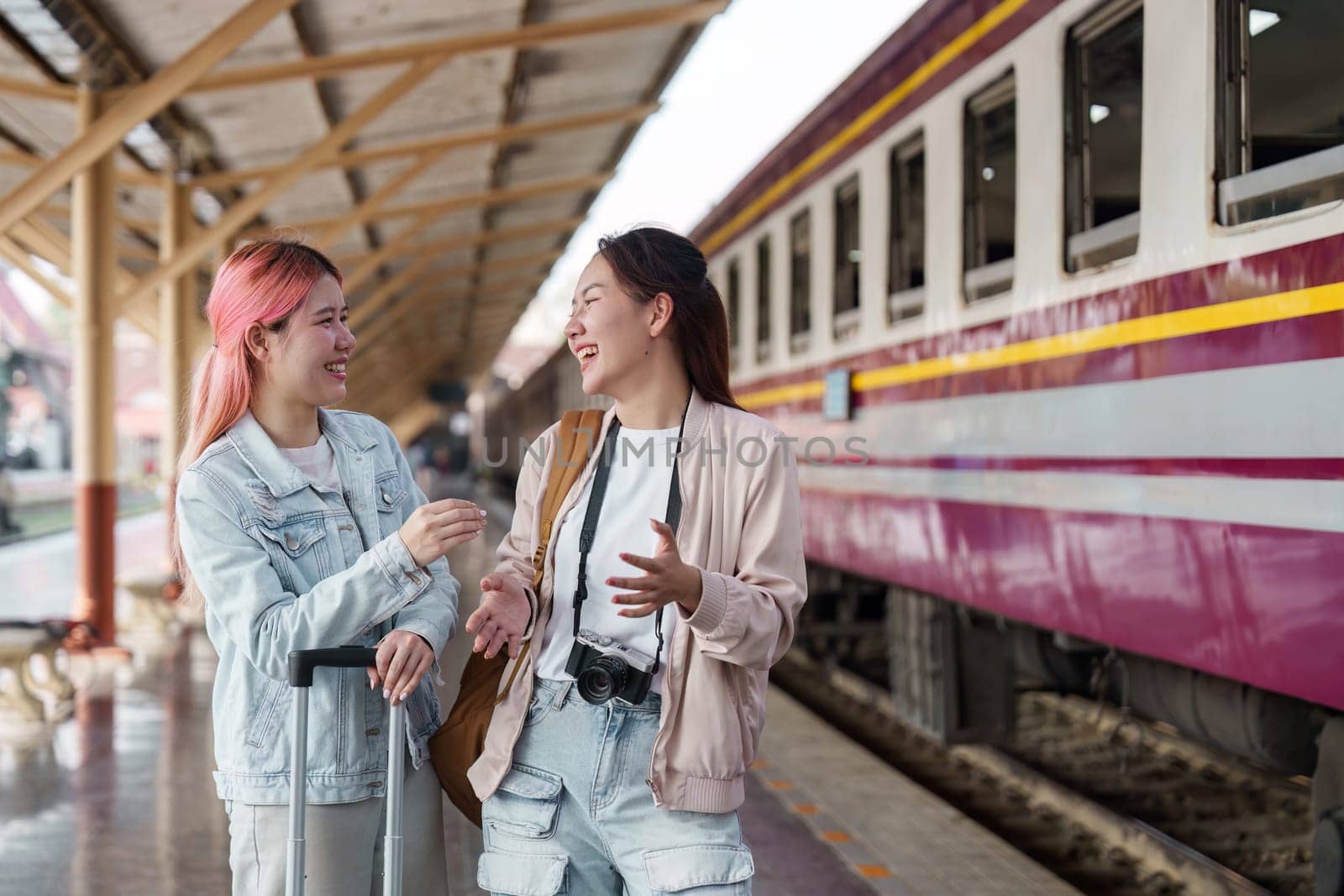 Two women converse animatedly at the train station, finding joy in each other's company as they prepare to embark on their trip.