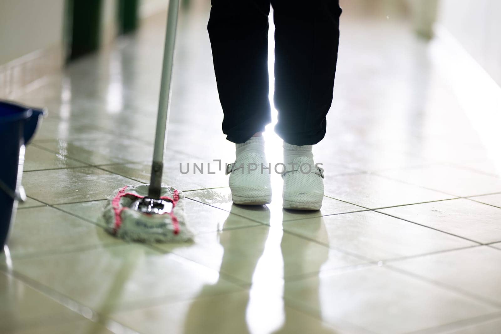 Female janitor standing in a hospital corridor with mop and bucket, symbolizing cleanliness and hygiene.