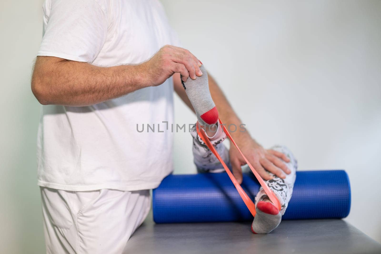 Therapist assisting with leg stretching using a resistance band during physical rehabilitation therapy session.