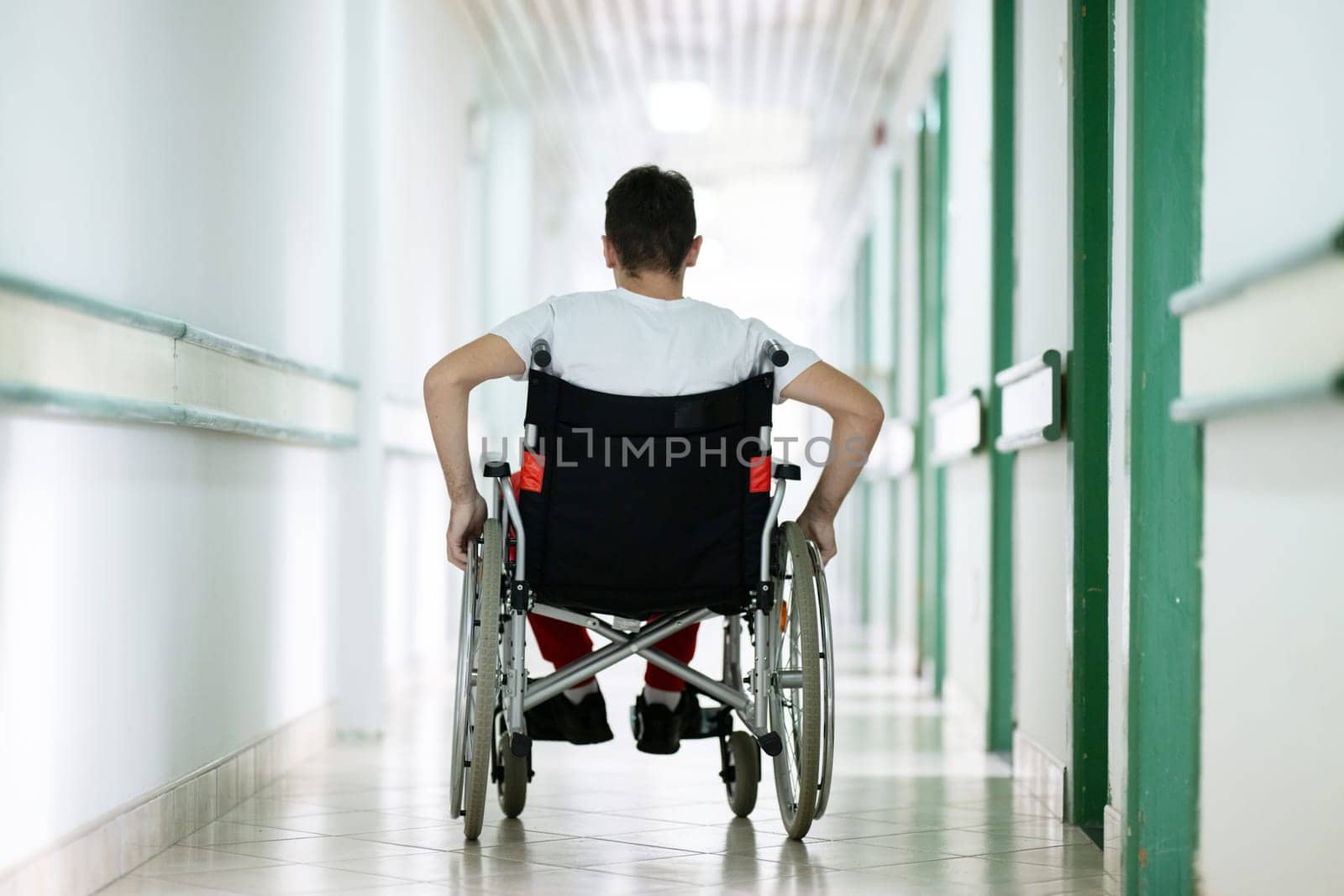 Young teenage boy smiling while sitting in a wheelchair in a hospital hallway. Rehabilitation and positivity concept