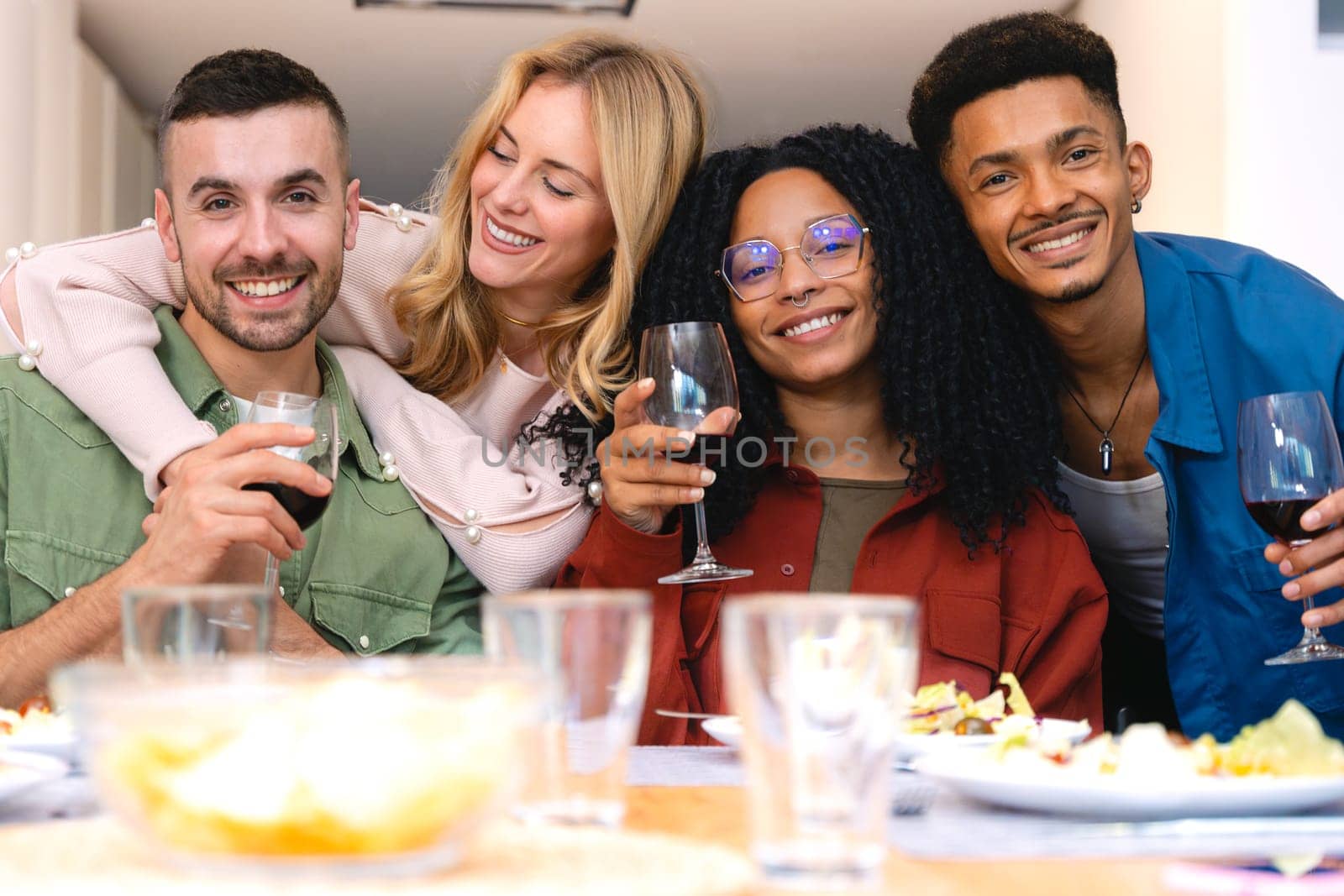 Group of multiethnic friends smiling at the camera while enjoying wine and dinner together at home. A joyful moment of connection, laughter, and celebration around a cozy and inviting table.