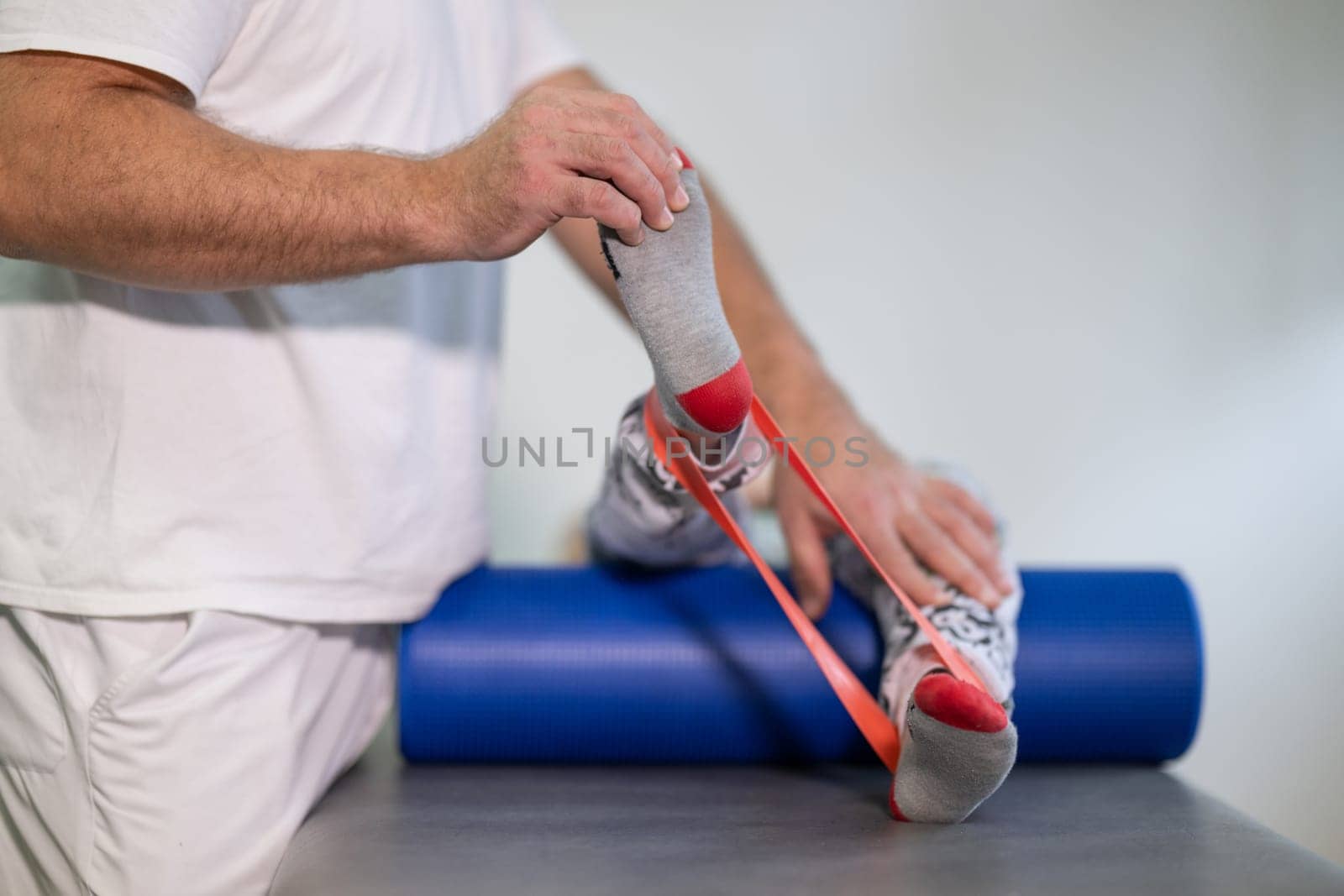Therapist assisting with leg stretching using a resistance band during physical rehabilitation therapy session.