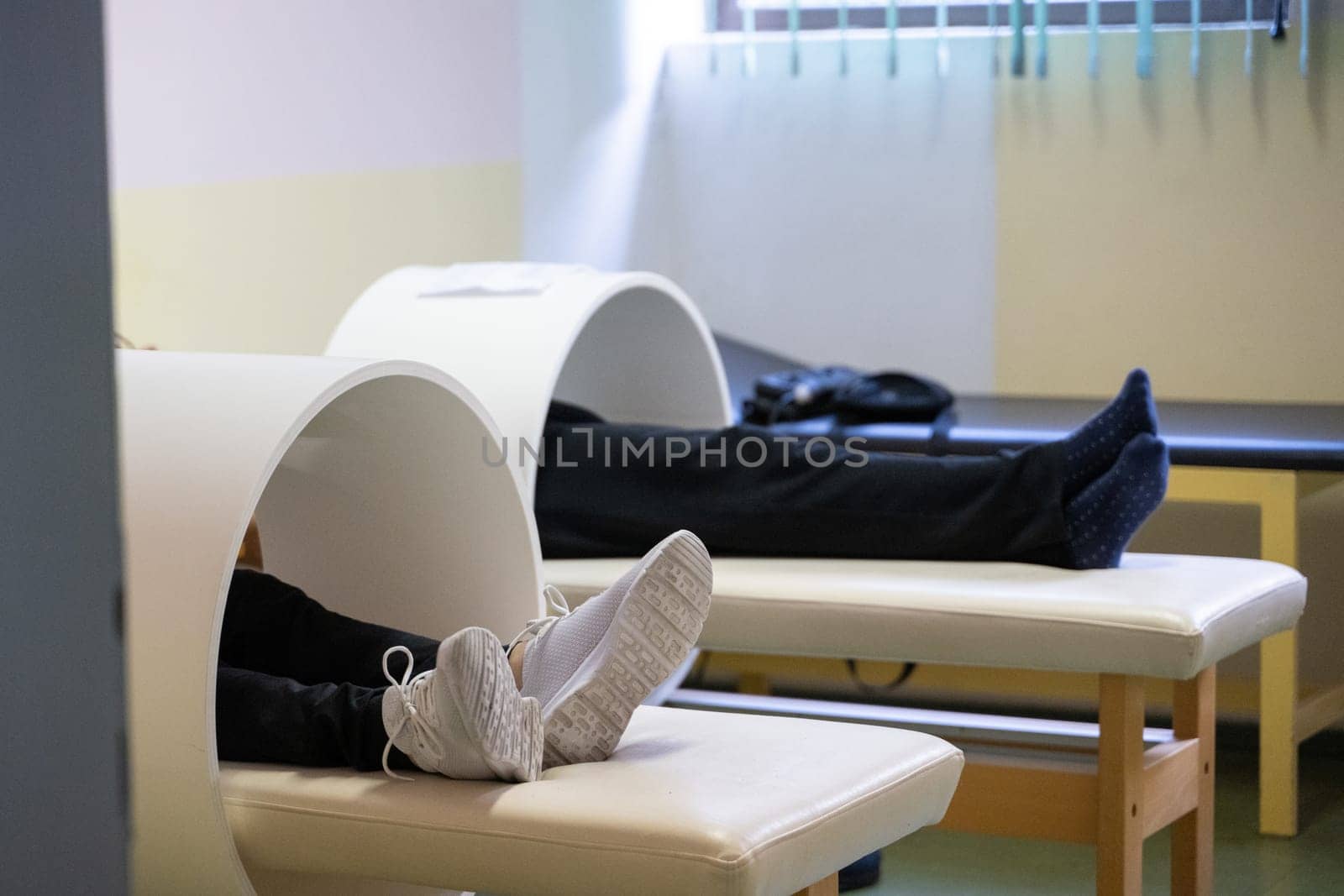 Patients lying down with legs inside circular magnetic therapy devices during a physiotherapy session.