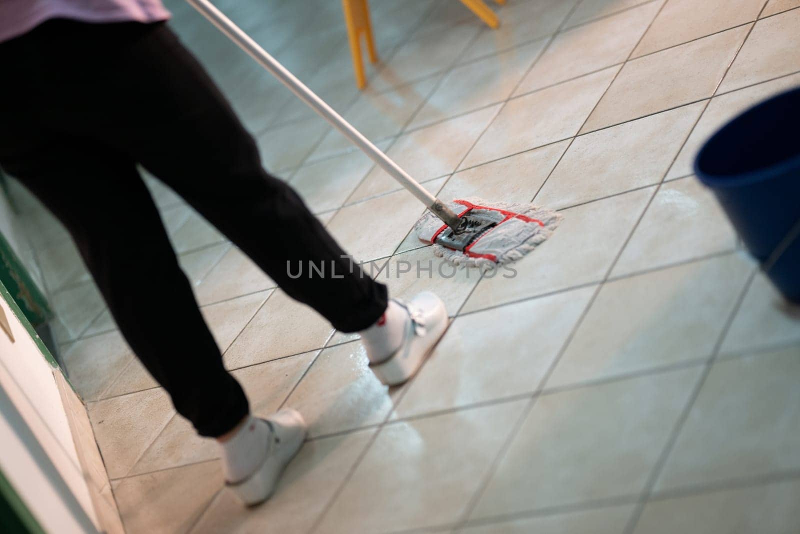 Female janitor standing in a hospital corridor with mop and bucket, symbolizing cleanliness and hygiene.