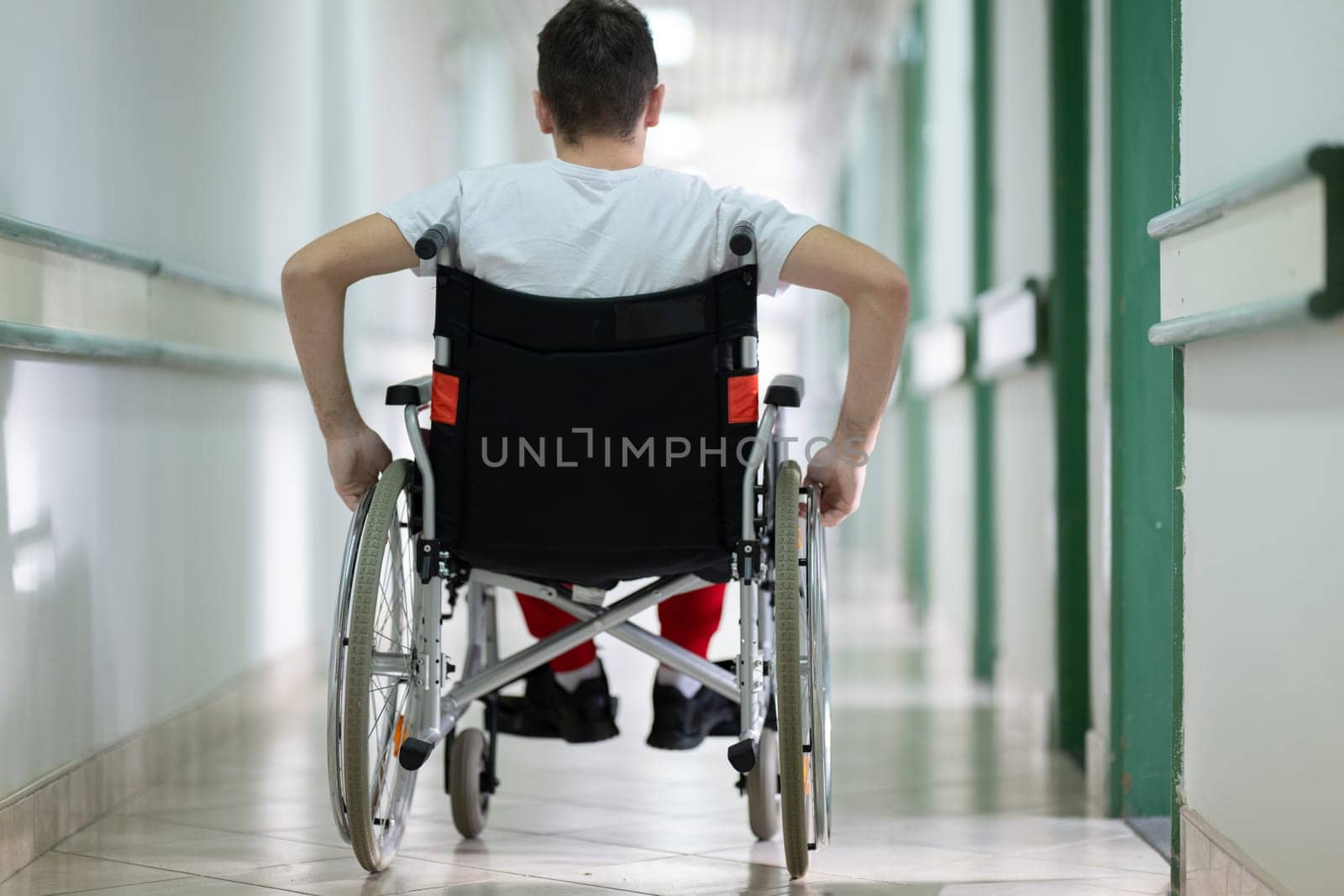 Young teenage boy smiling while sitting in a wheelchair in a hospital hallway. Rehabilitation and positivity concept