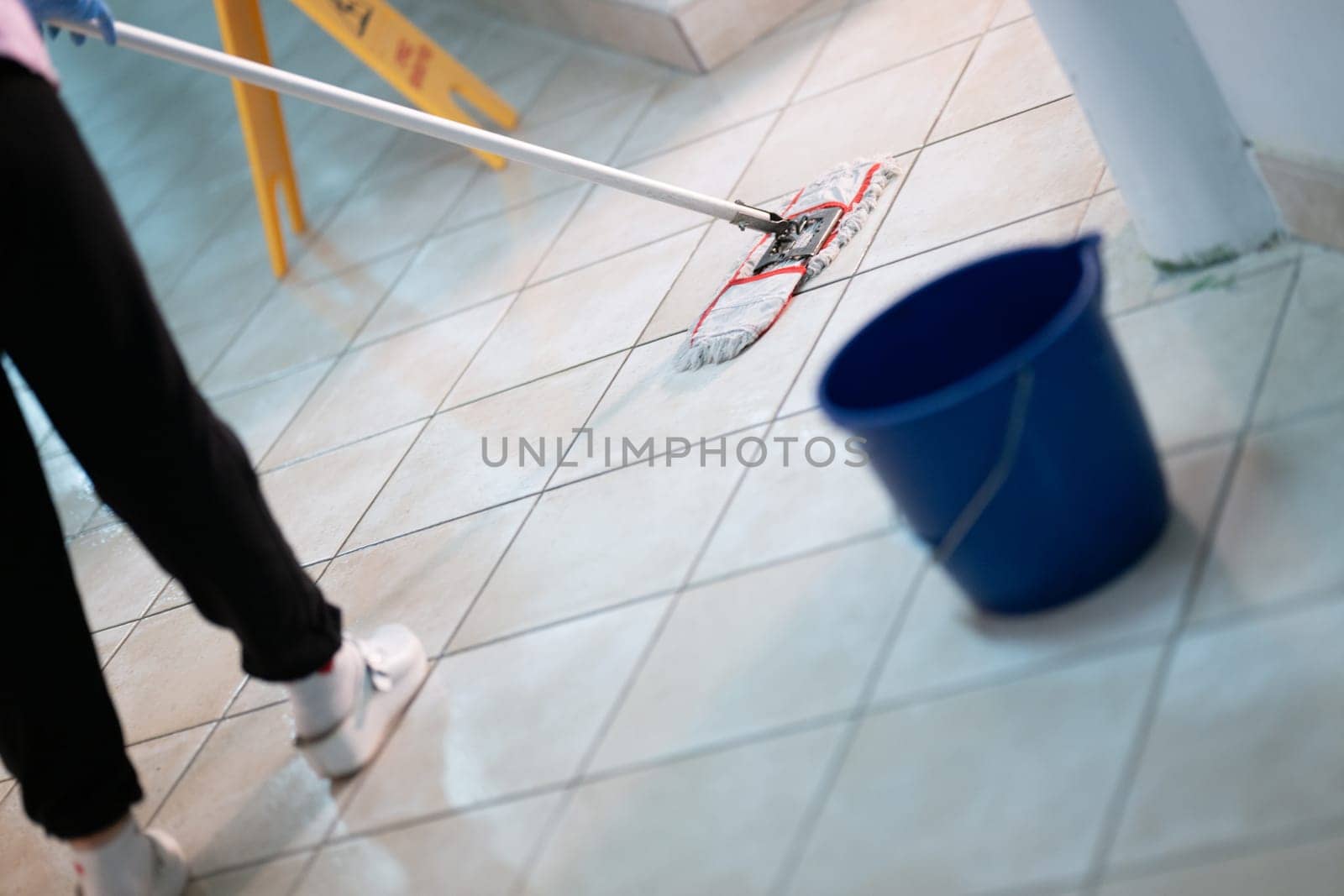 Female janitor standing in a hospital corridor with mop and bucket, symbolizing cleanliness and hygiene.