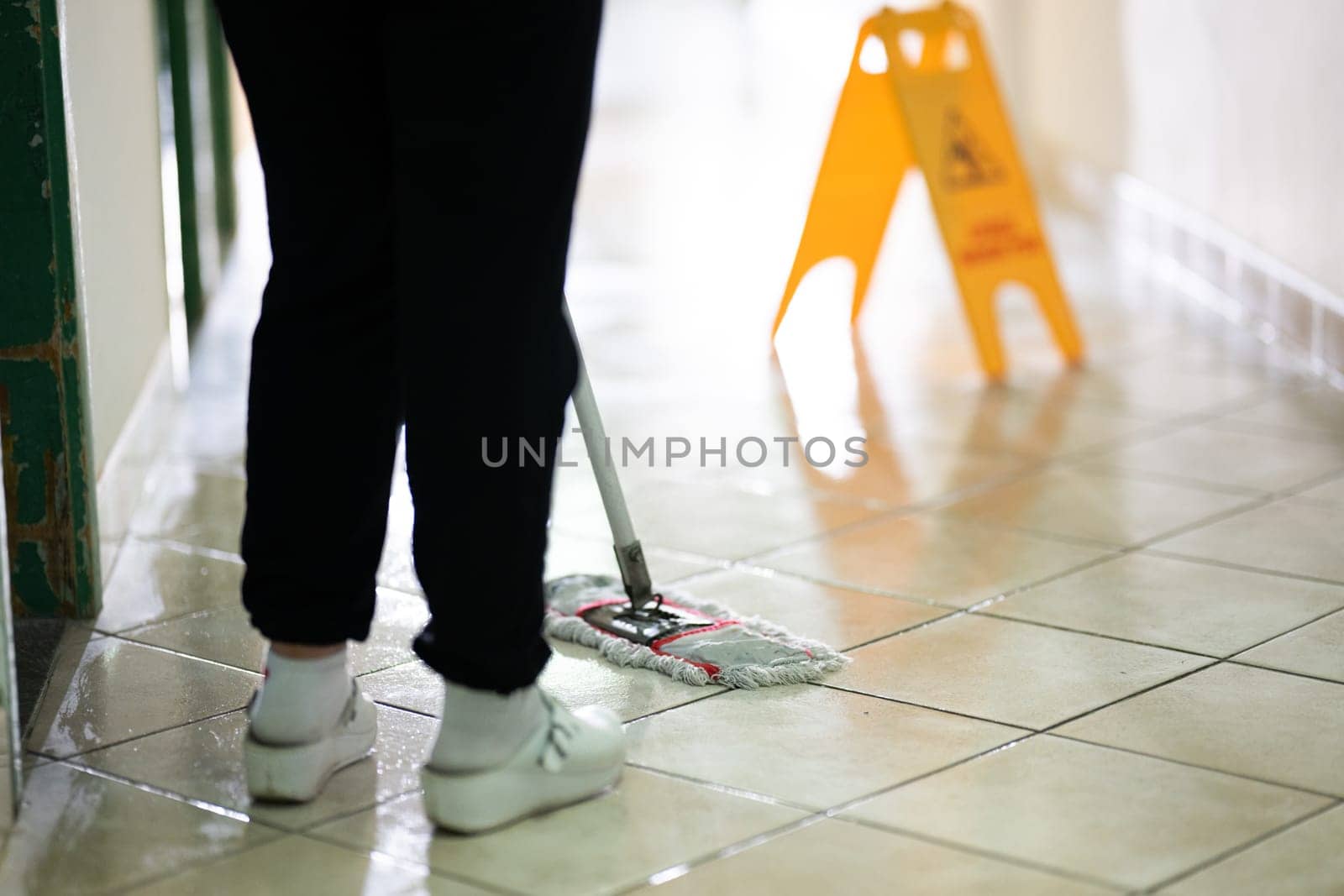 Female janitor standing in a hospital corridor with mop and bucket, symbolizing cleanliness and hygiene.