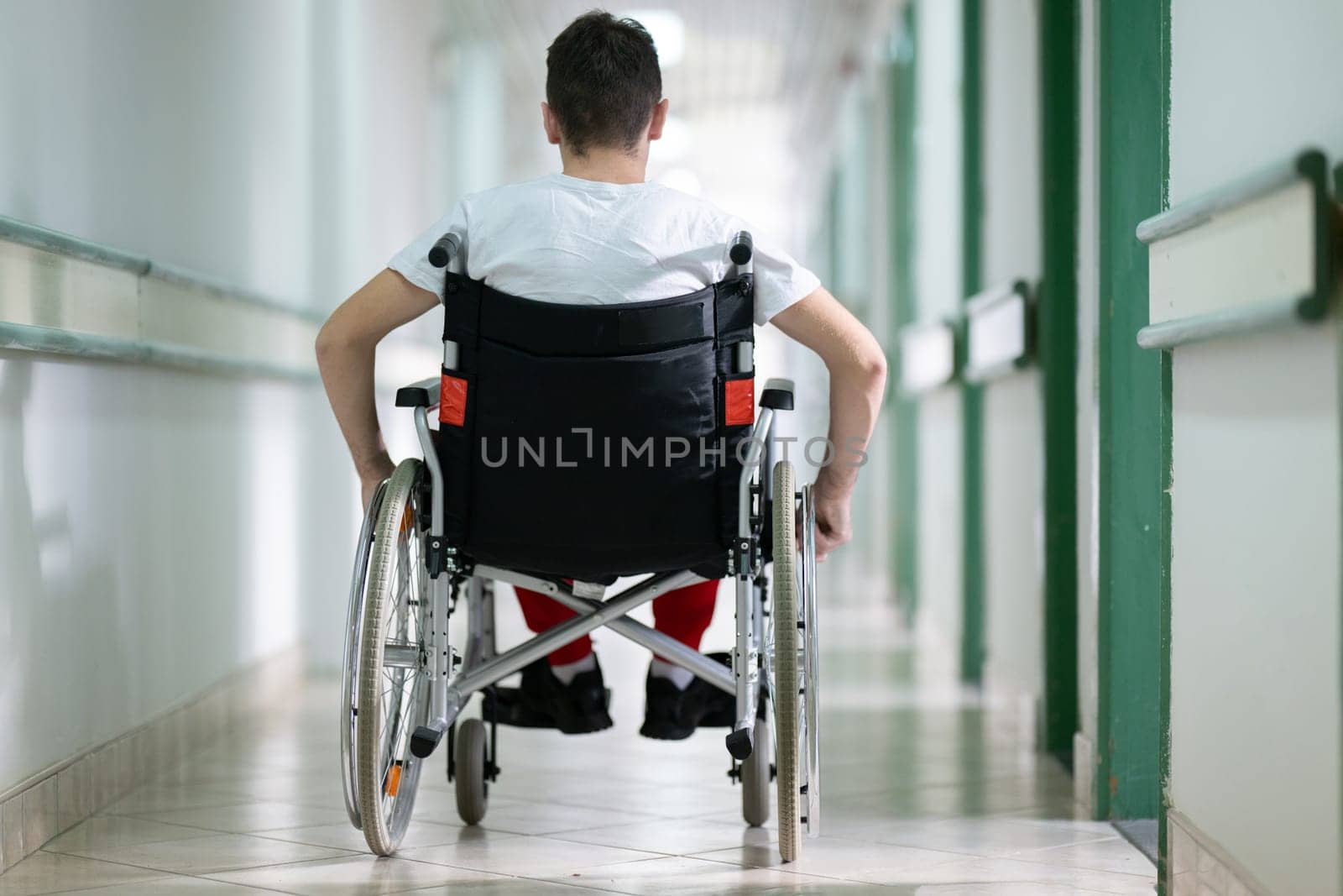 Young teenage boy smiling while sitting in a wheelchair in a hospital hallway. Rehabilitation and positivity concept
