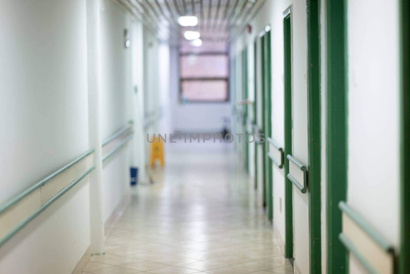 Bright and clean hospital corridor with green doors and handrails, illuminated by natural daylight through windows.