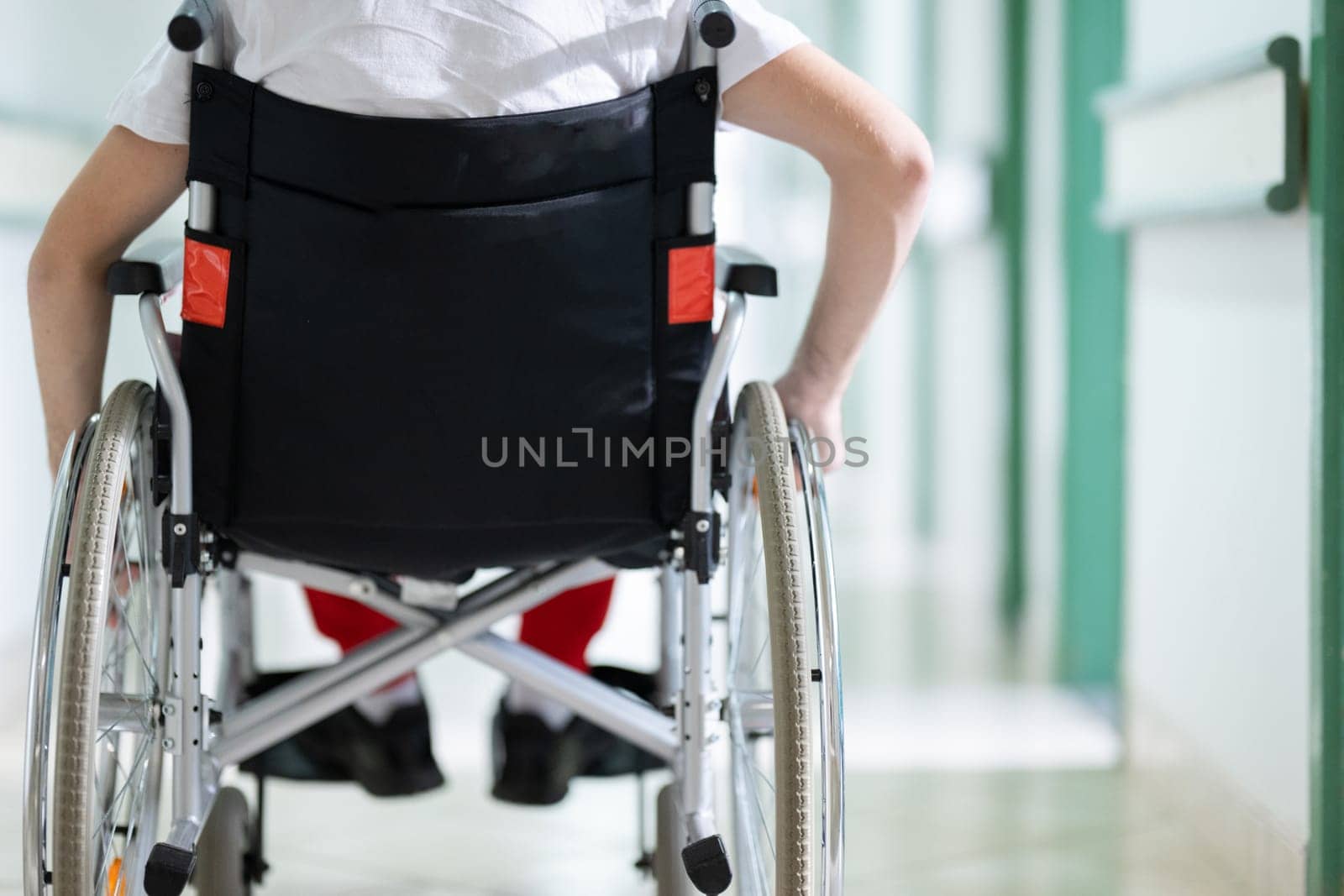 Young teenage boy smiling while sitting in a wheelchair in a hospital hallway. Rehabilitation and positivity concept