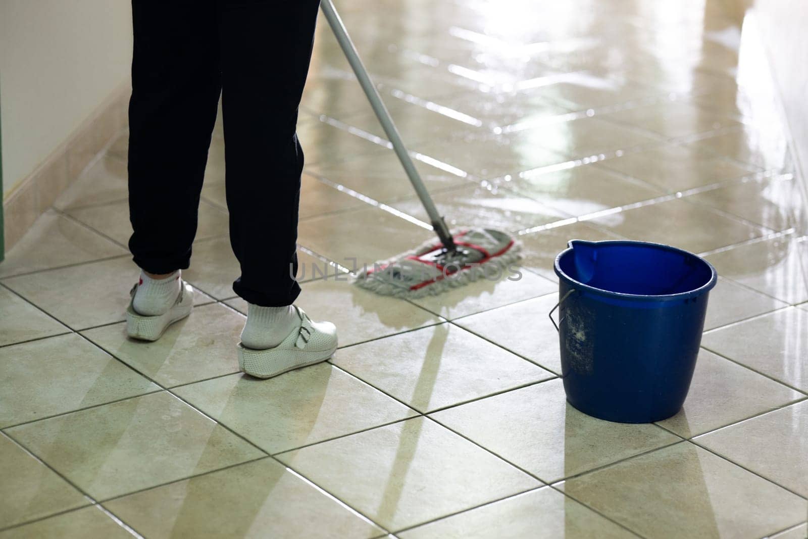 Female janitor standing in a hospital corridor with mop and bucket, symbolizing cleanliness and hygiene.