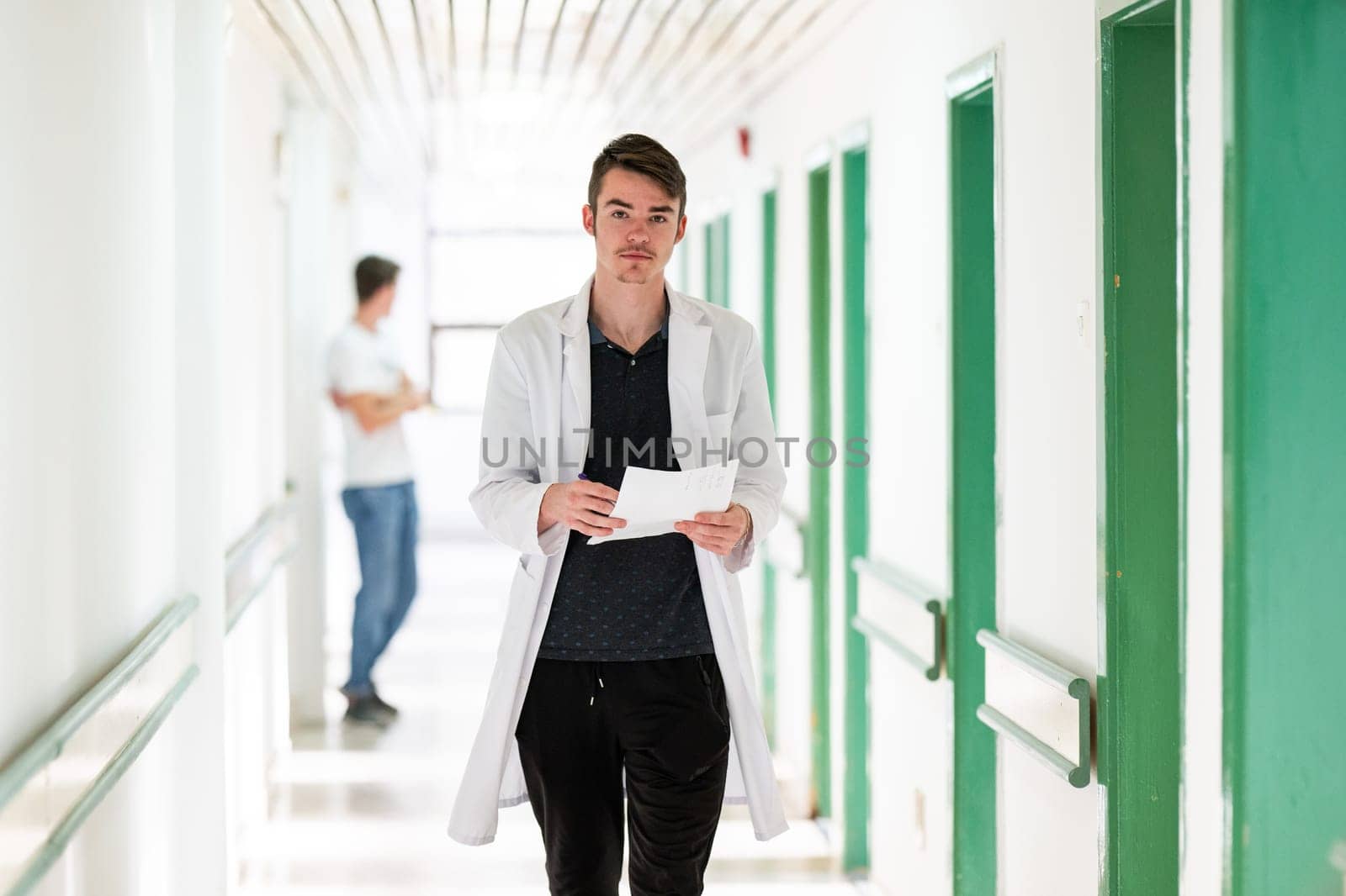 Young male doctor walking in hospital hallway while reading patient documentation. Clinical work environment.