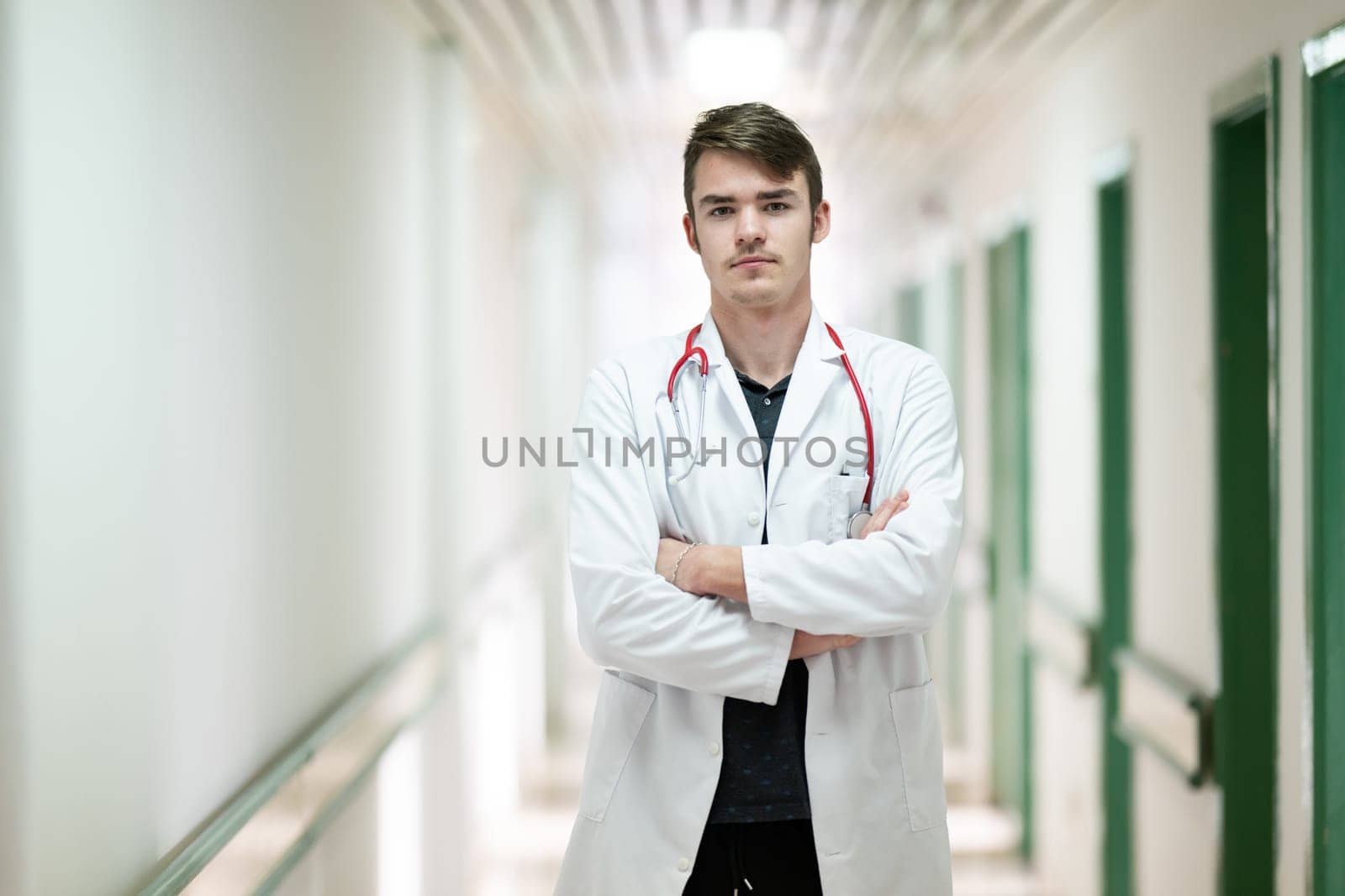 Young male doctor standing confidently in a hospital corridor with a stethoscope. Medical professionalism concept.