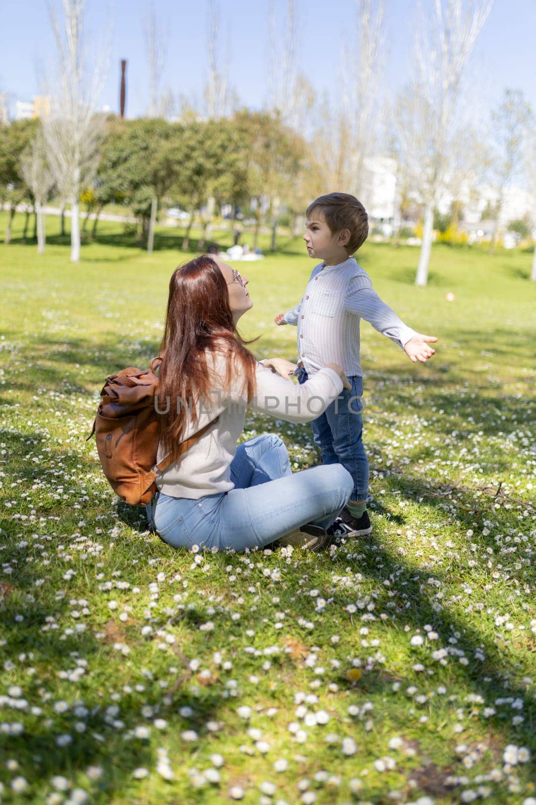 Mother sitting on the grass interacting with her son in a park full of daisies