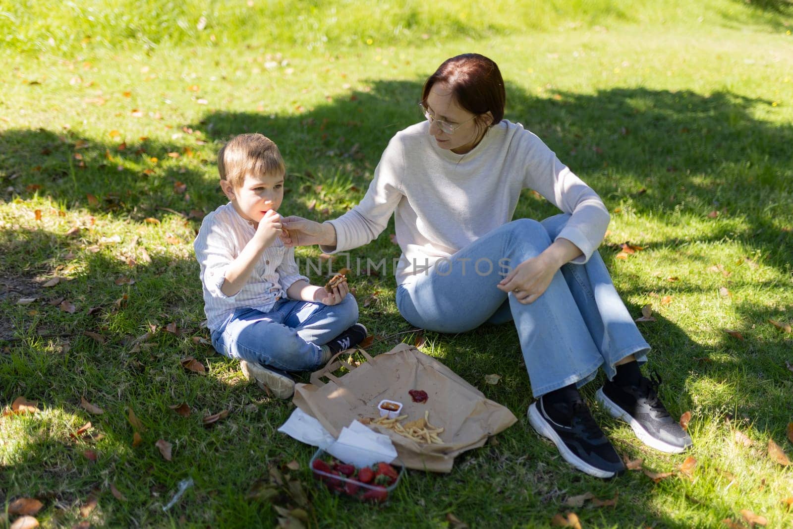 Mother and son sharing a pleasant moment during a picnic in a park, eating french fries and strawberries