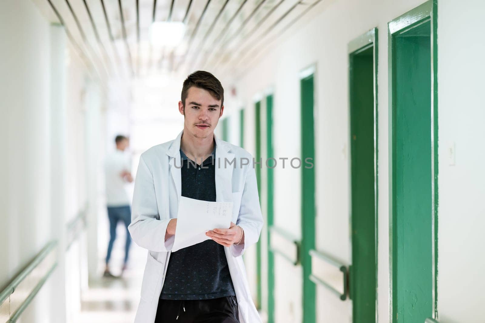Young male doctor walking in hospital hallway while reading patient documentation. Clinical work environment.