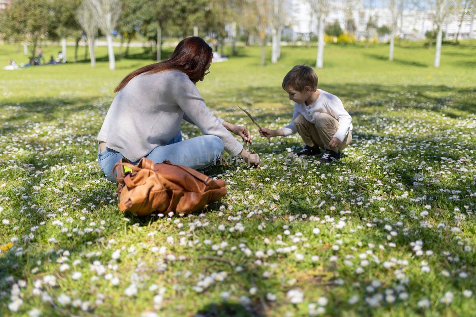 Mother and son enjoying a sunny spring day picking daisies in a park