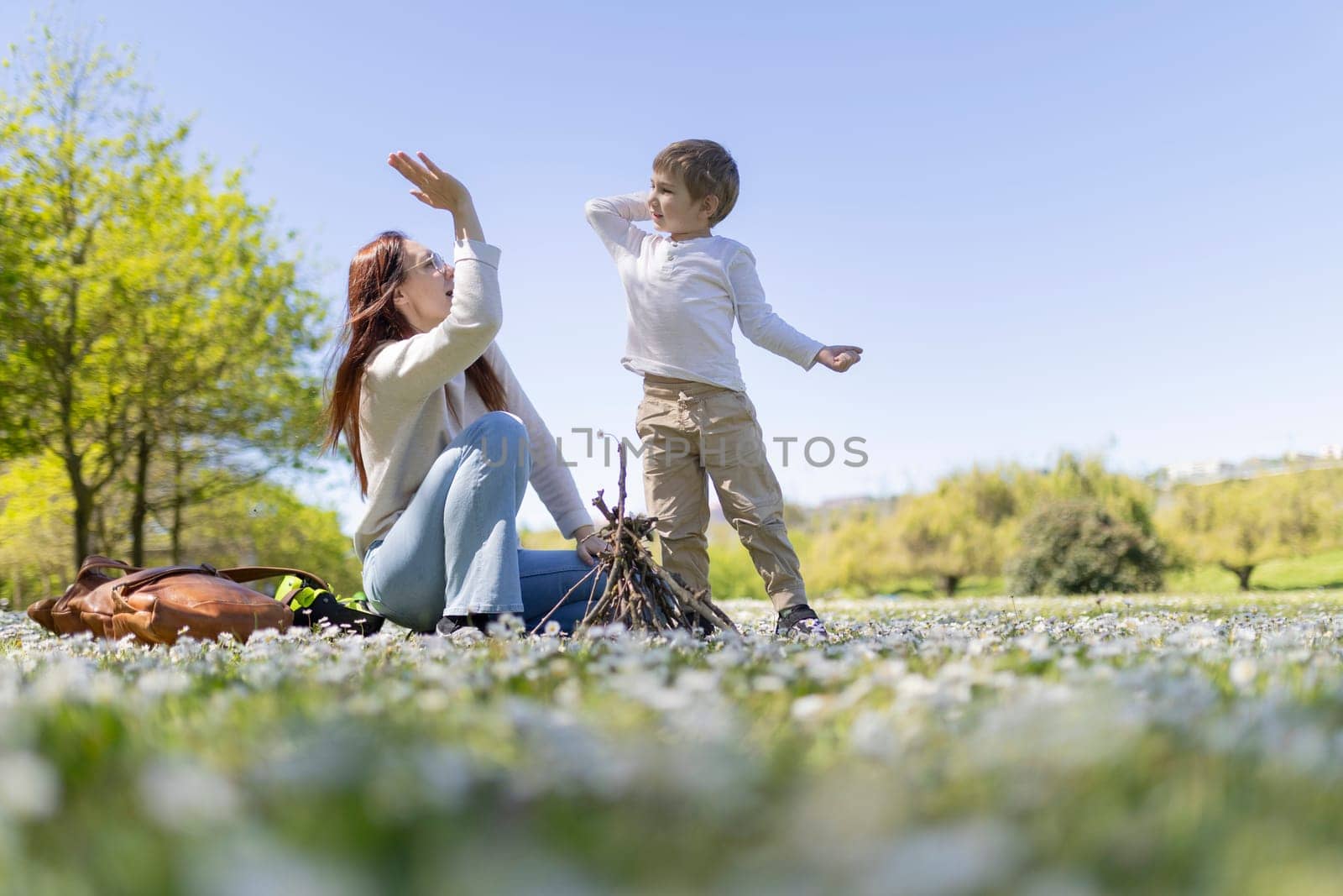 Mother and son having fun in a field of flowers, preparing to build a campfire on a sunny day