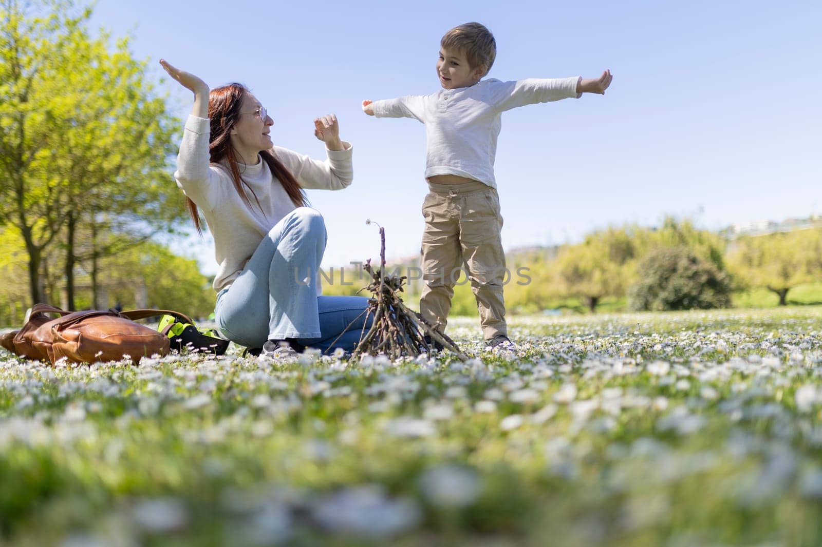 Mother and son are playing in a field of flowers and building a small bonfire on a sunny day