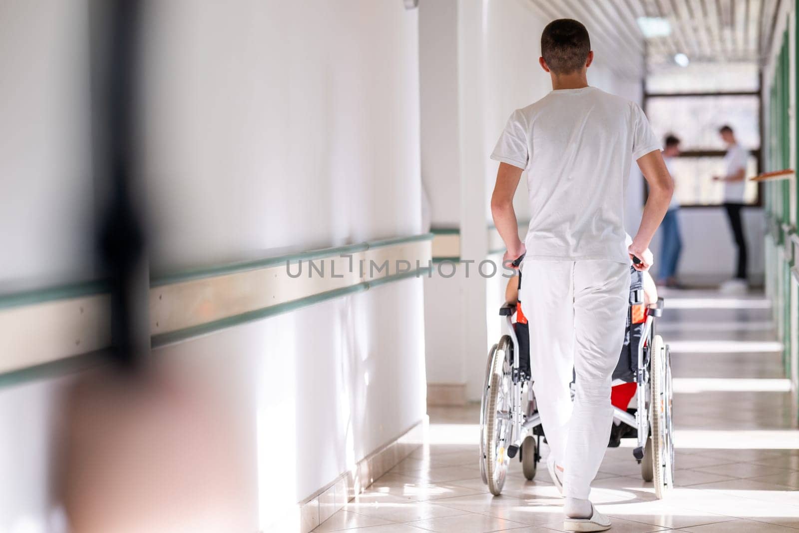 Medical staff in white uniforms assist a patient in a wheelchair in a bright hospital corridor. Concept of healthcare and assistance.