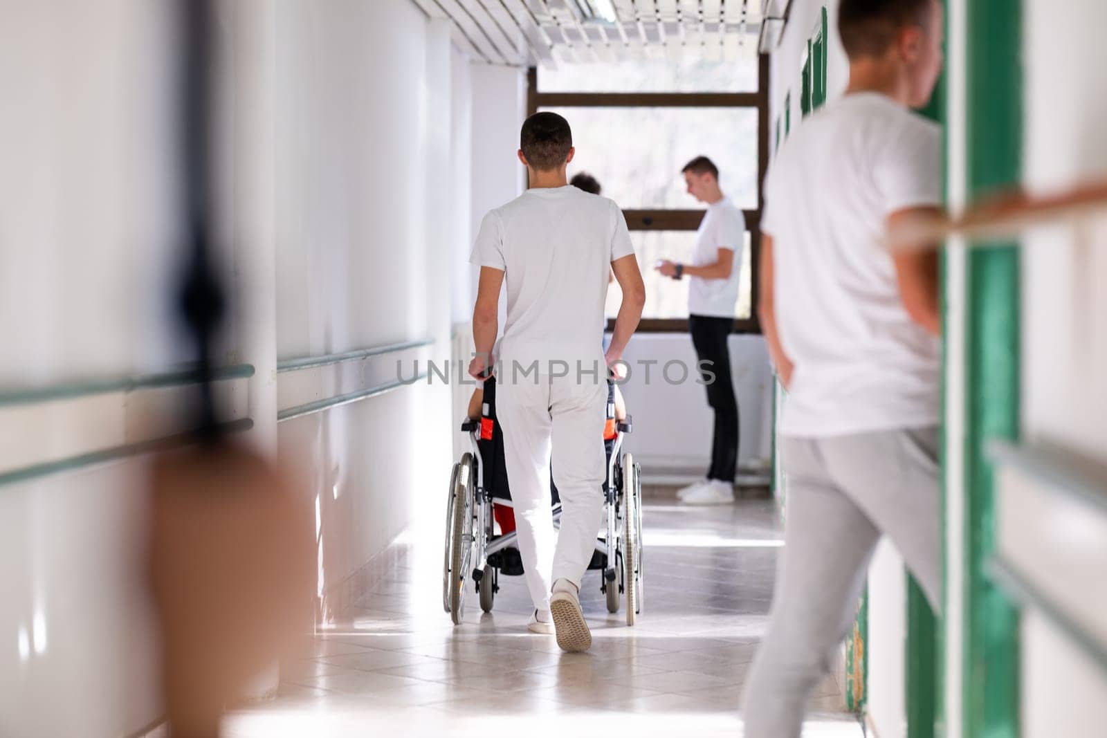 Medical staff in white uniforms assist a patient in a wheelchair in a bright hospital corridor. Concept of healthcare and assistance.