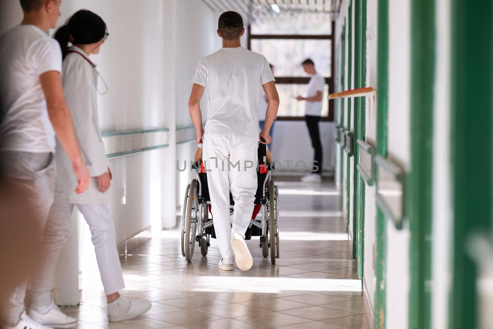 Medical staff in white uniforms assist a patient in a wheelchair in a bright hospital corridor. Concept of healthcare and assistance.