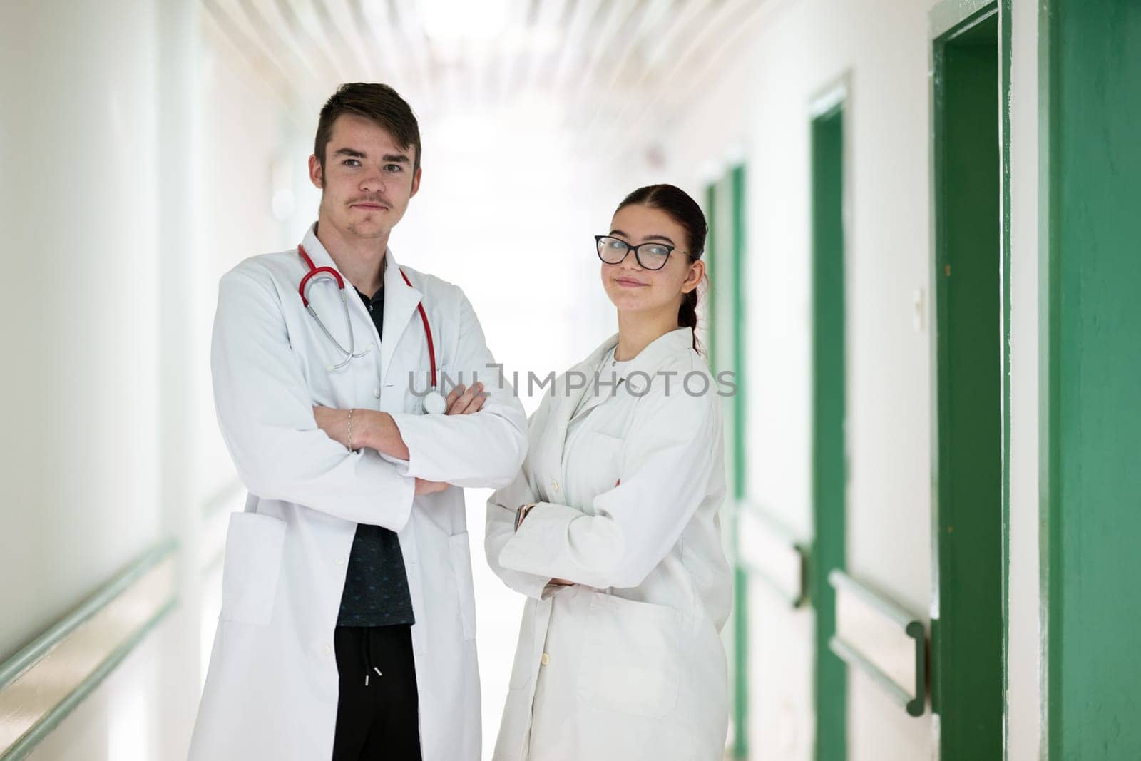 Male and female doctors in white coats posing confidently in hospital hallway. Teamwork and healthcare concept.