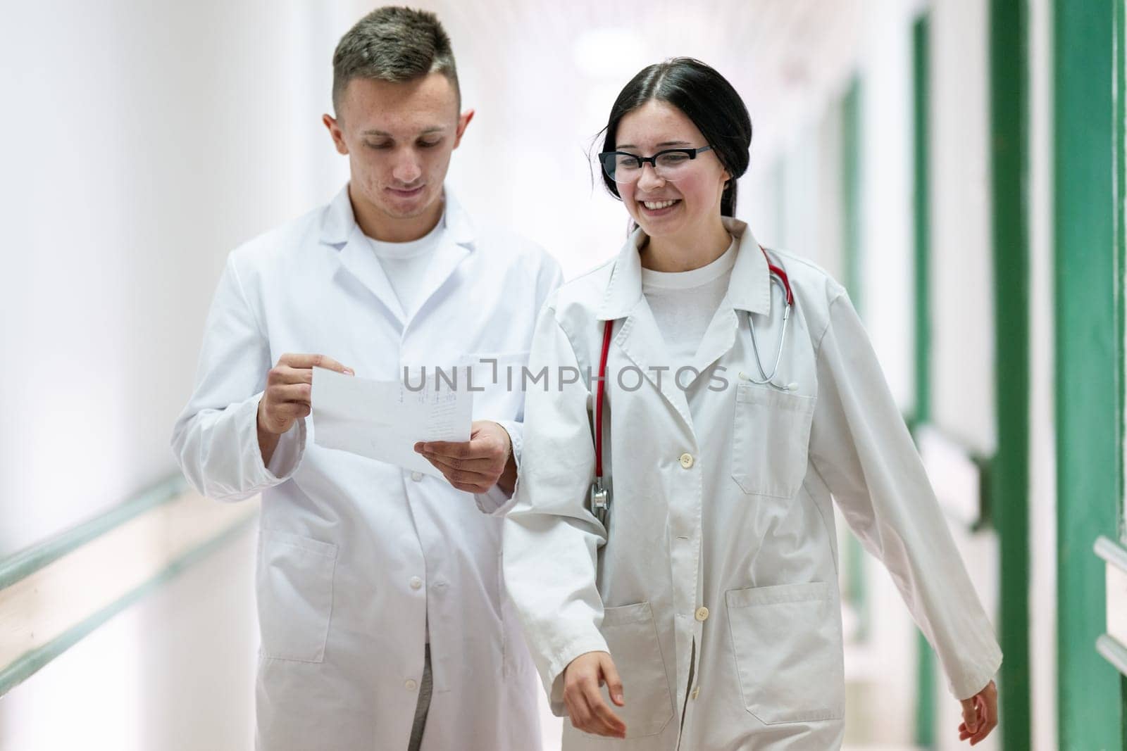 Two doctors in white coats walking and discussing medical documents in a brightly lit hospital corridor, emphasizing teamwork and professional healthcare environment.