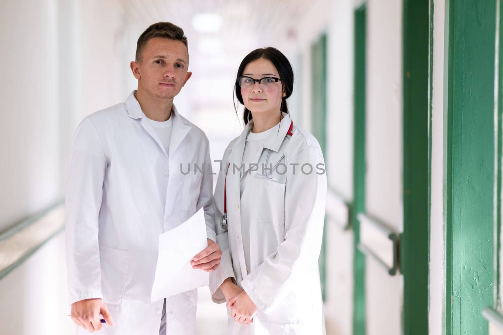 Two doctors in white coats walking and discussing medical documents in a brightly lit hospital corridor, emphasizing teamwork and professional healthcare environment.