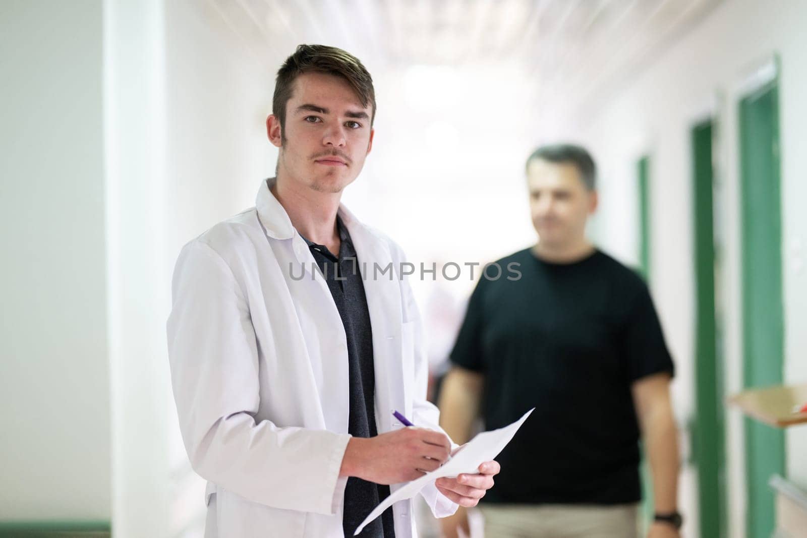 Young male doctor walking in hospital hallway while reading patient documentation. Clinical work environment.