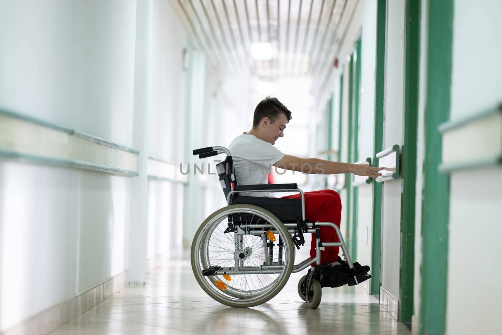 Young teenage boy smiling while sitting in a wheelchair in a hospital hallway. Rehabilitation and positivity concept