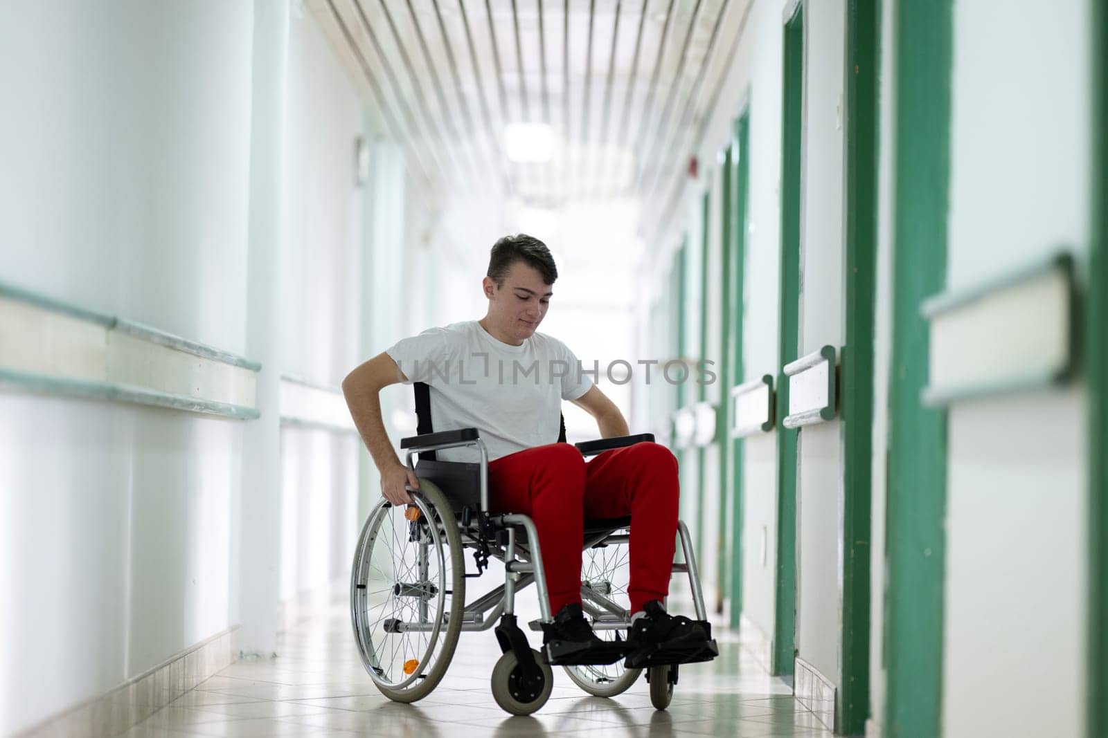 Young teenage boy smiling while sitting in a wheelchair in a hospital hallway. Rehabilitation and positivity concept