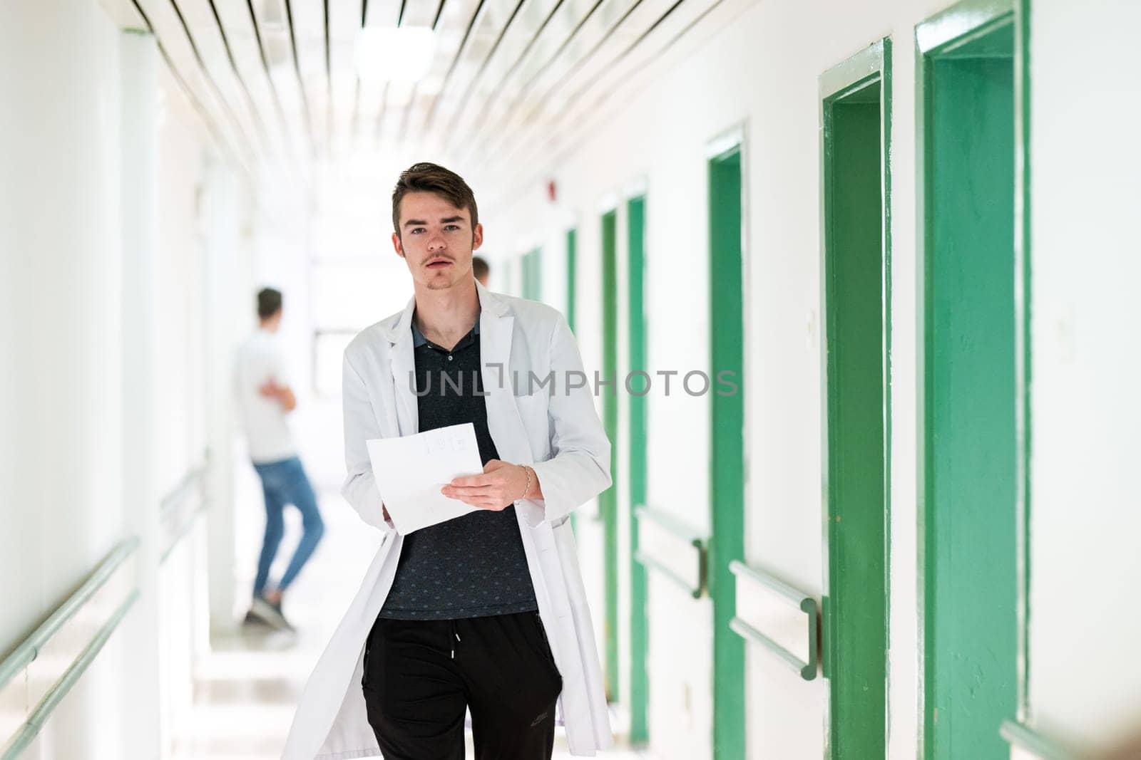 Young male doctor walking in hospital hallway while reading patient documentation. Clinical work environment.