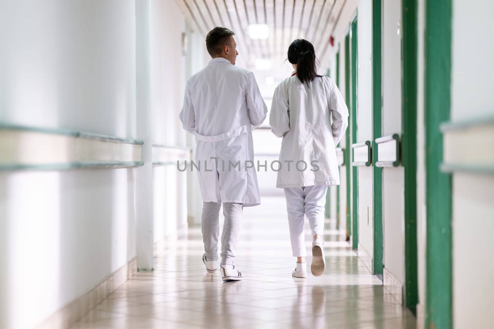Two doctors in white coats walking and discussing medical documents in a brightly lit hospital corridor, emphasizing teamwork and professional healthcare environment.