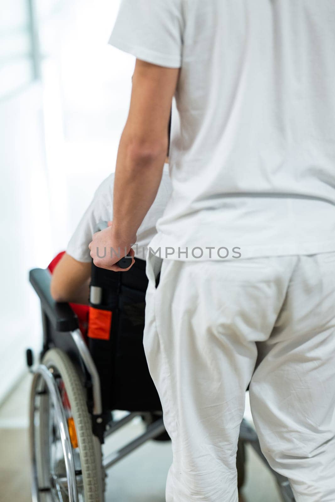 Medical staff in white uniforms assist a patient in a wheelchair in a bright hospital corridor. Concept of healthcare and assistance.