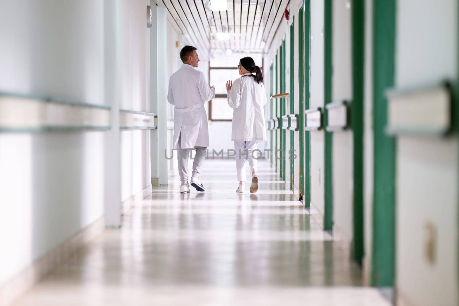 Two doctors in white coats walking and discussing medical documents in a brightly lit hospital corridor, emphasizing teamwork and professional healthcare environment.