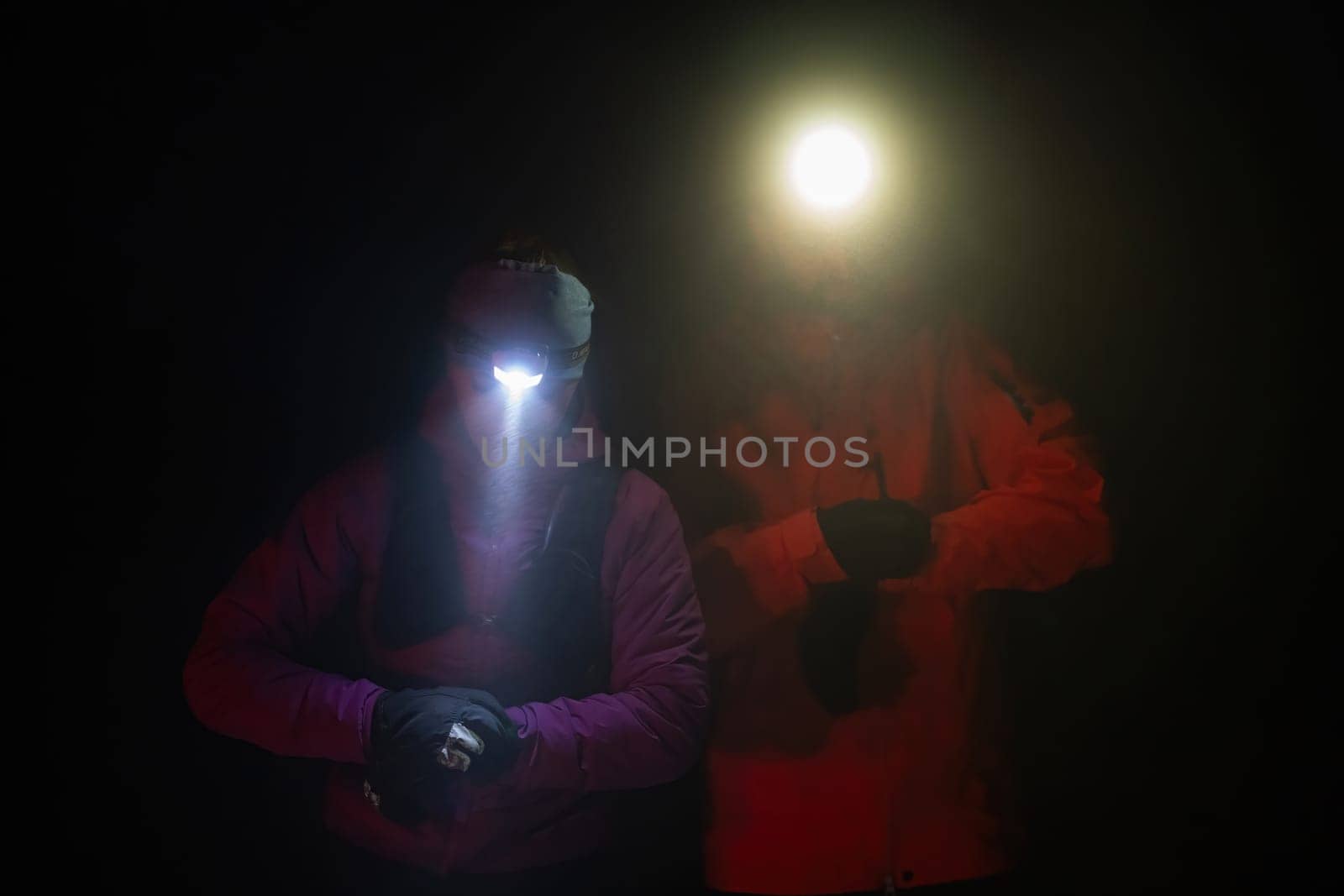 Couple equipped with headlamps explore a forest in total darkness, with beams of light cutting through the night air.