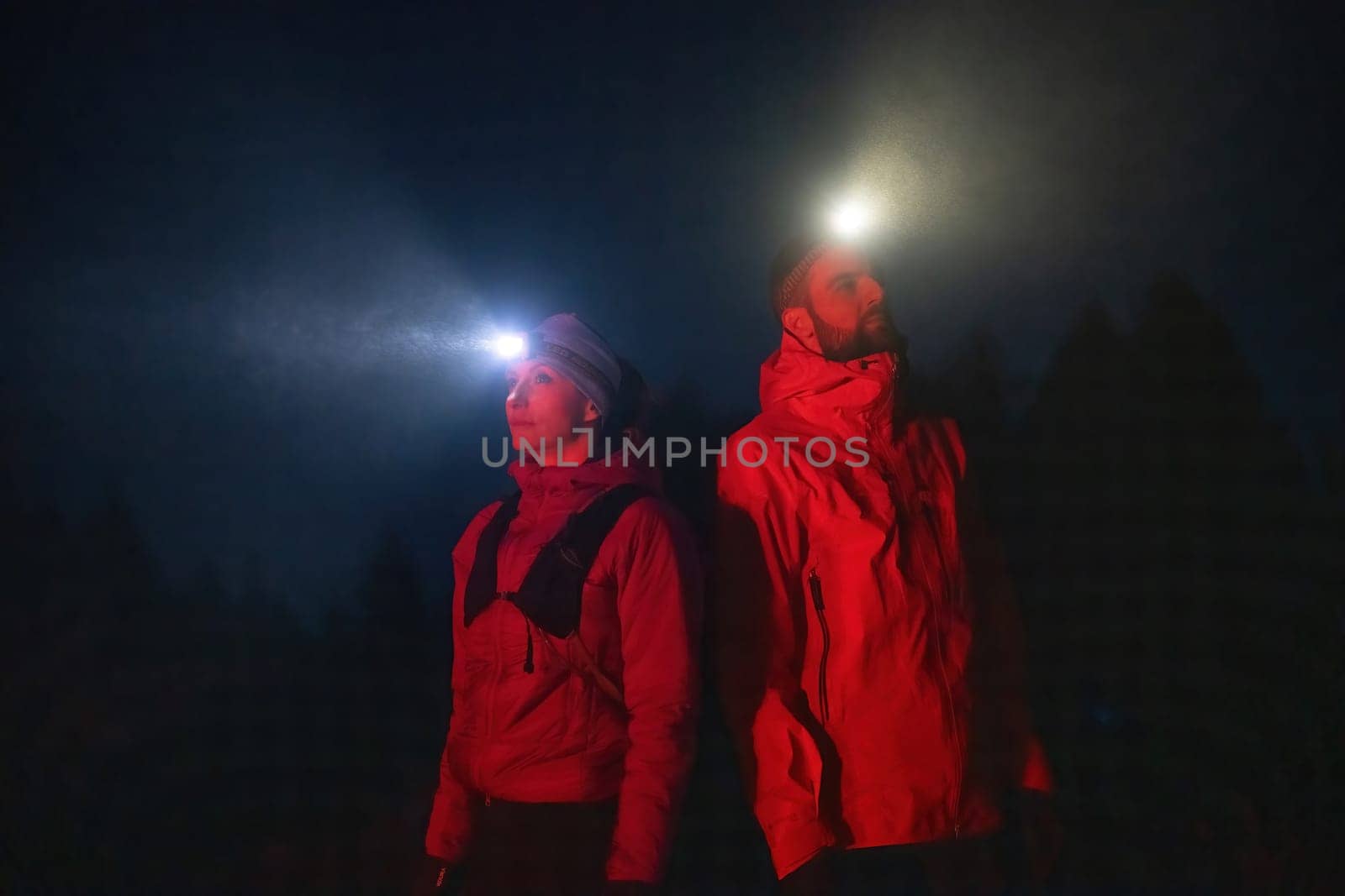 Couple equipped with headlamps explore a forest in total darkness, with beams of light cutting through the night air.