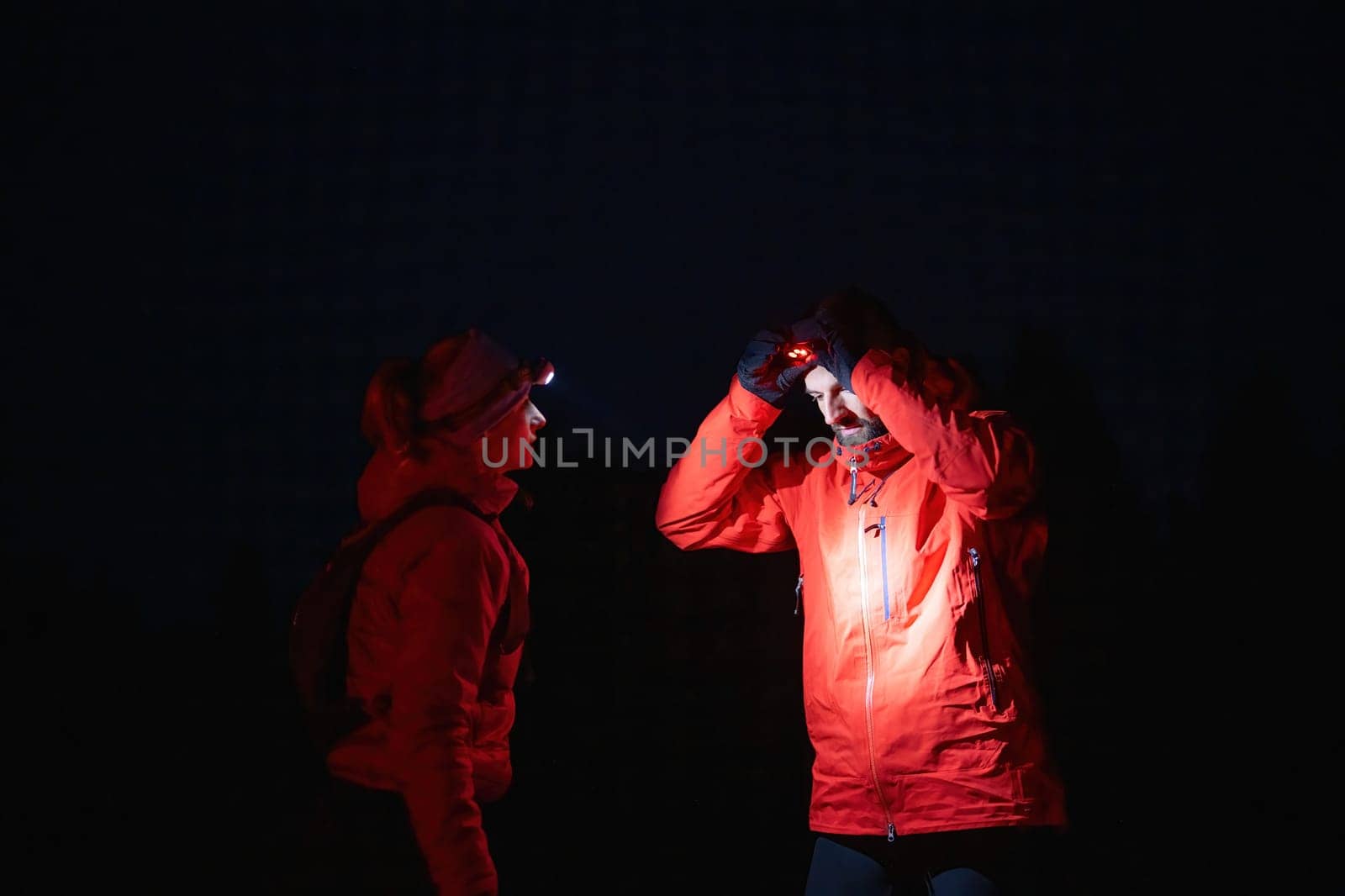 Couple equipped with headlamps explore a forest in total darkness, with beams of light cutting through the night air.