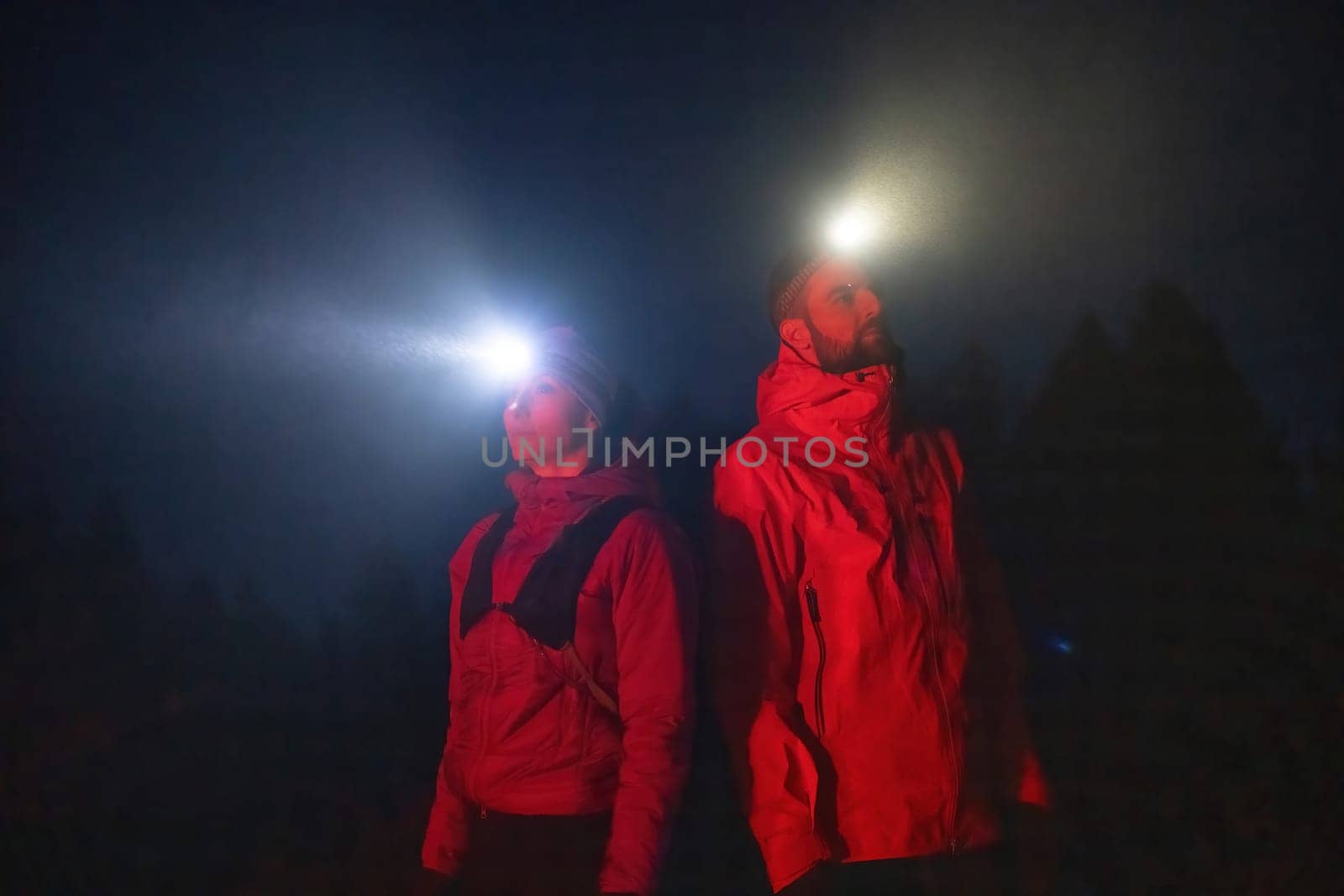 Couple equipped with headlamps explore a forest in total darkness, with beams of light cutting through the night air.