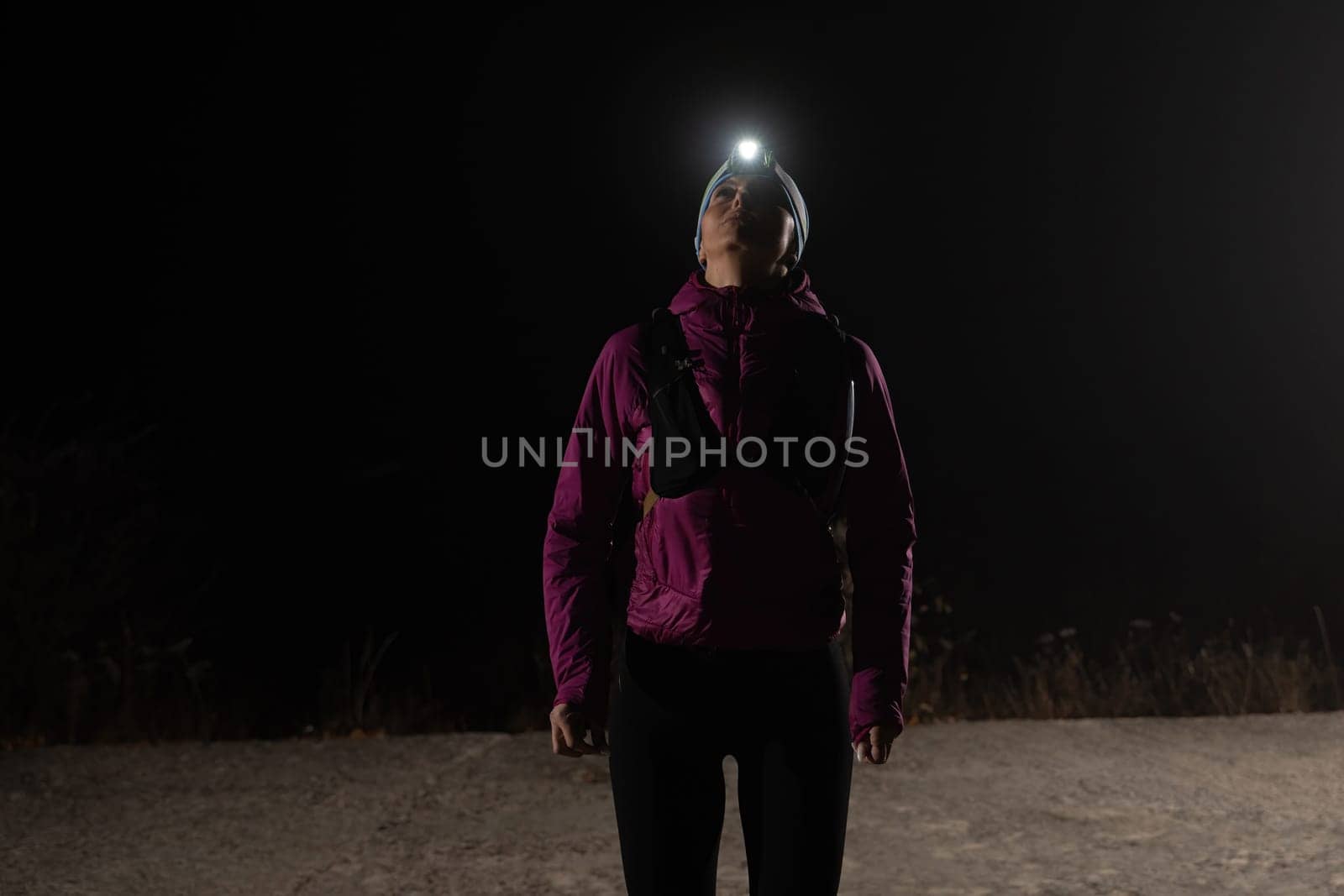 Woman jogging at night with headlamp on, captured in dark outdoor environment.