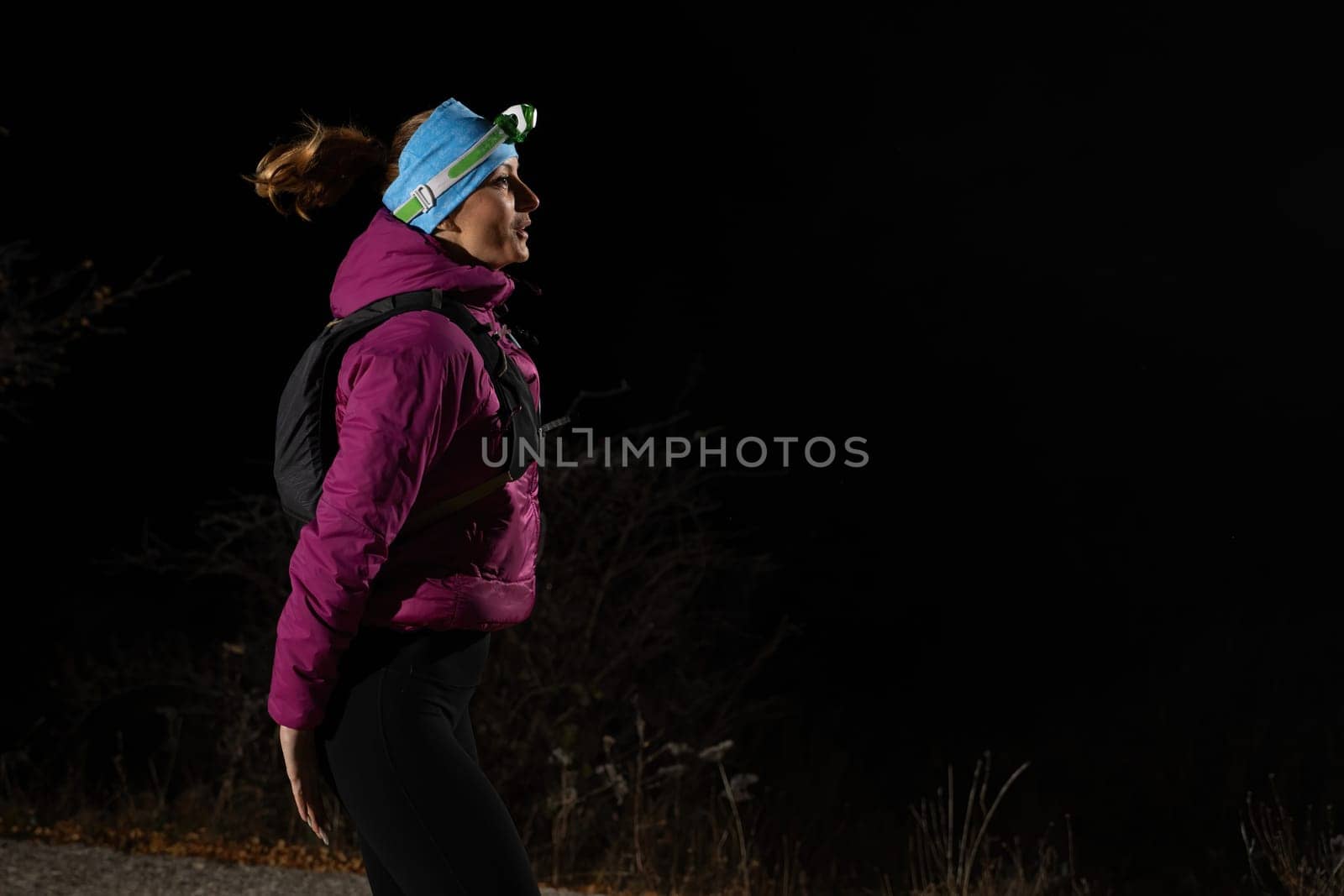 Woman jogging at night with headlamp on, captured in dark outdoor environment.