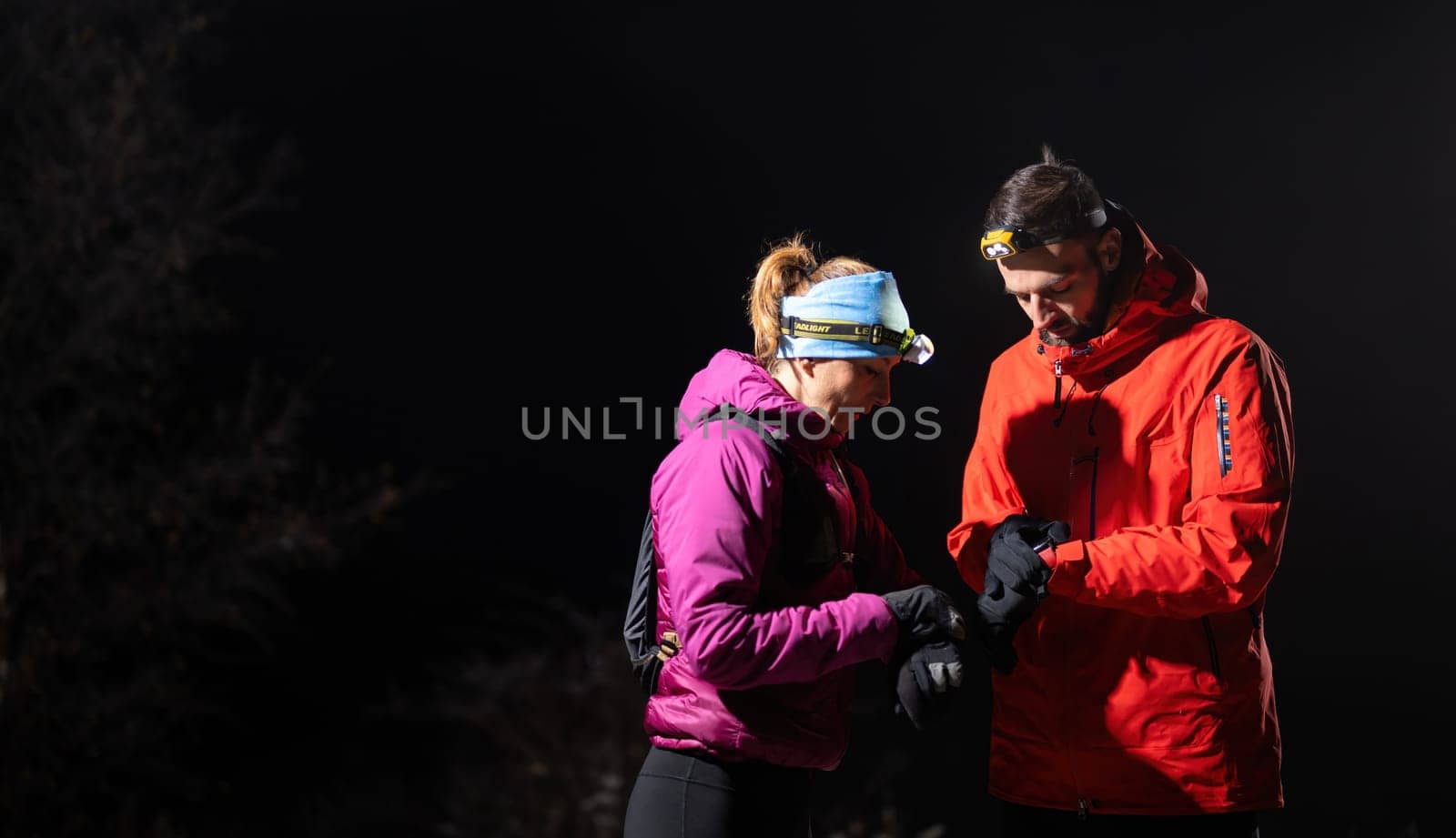 Couple night hikers examine a device under headlamp light, emphasizing navigation and teamwork under low light conditions.