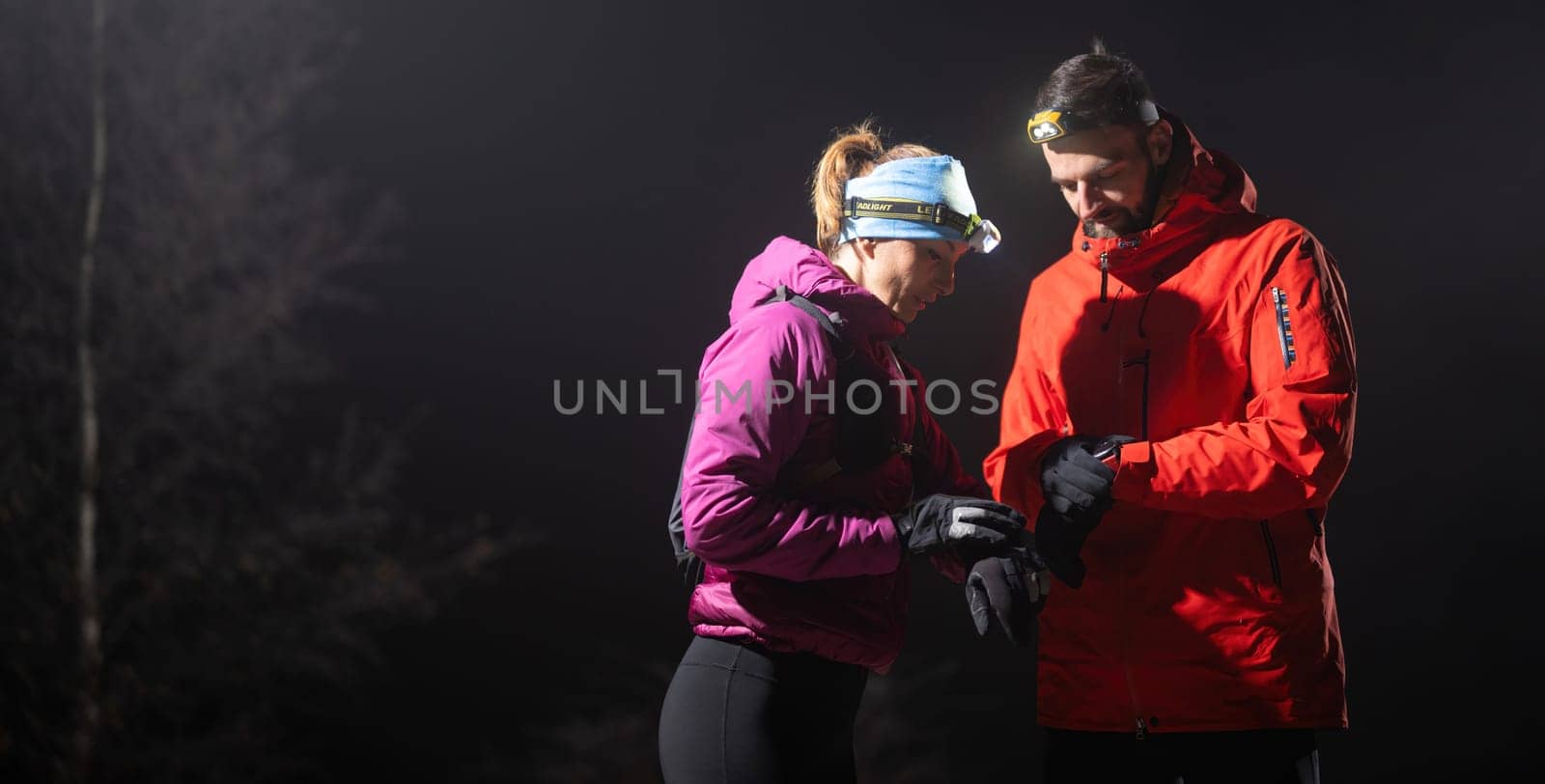 Couple night hikers examine a device under headlamp light, emphasizing navigation and teamwork under low light conditions.