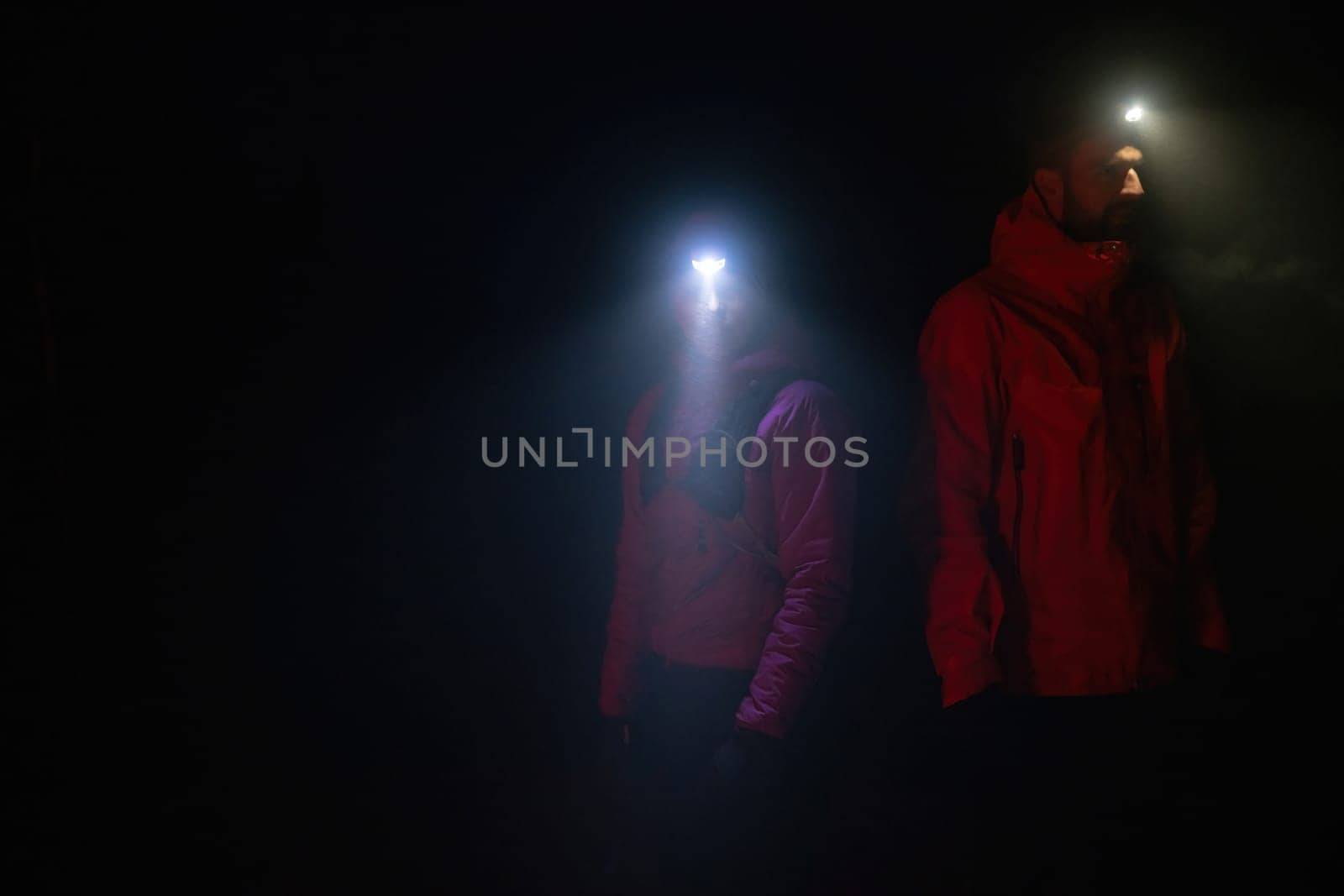 Couple equipped with headlamps explore a forest in total darkness, with beams of light cutting through the night air.