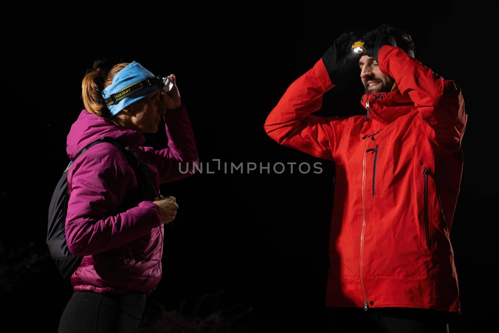 Couple equipped with headlamps explore a forest in total darkness, with beams of light cutting through the night air.