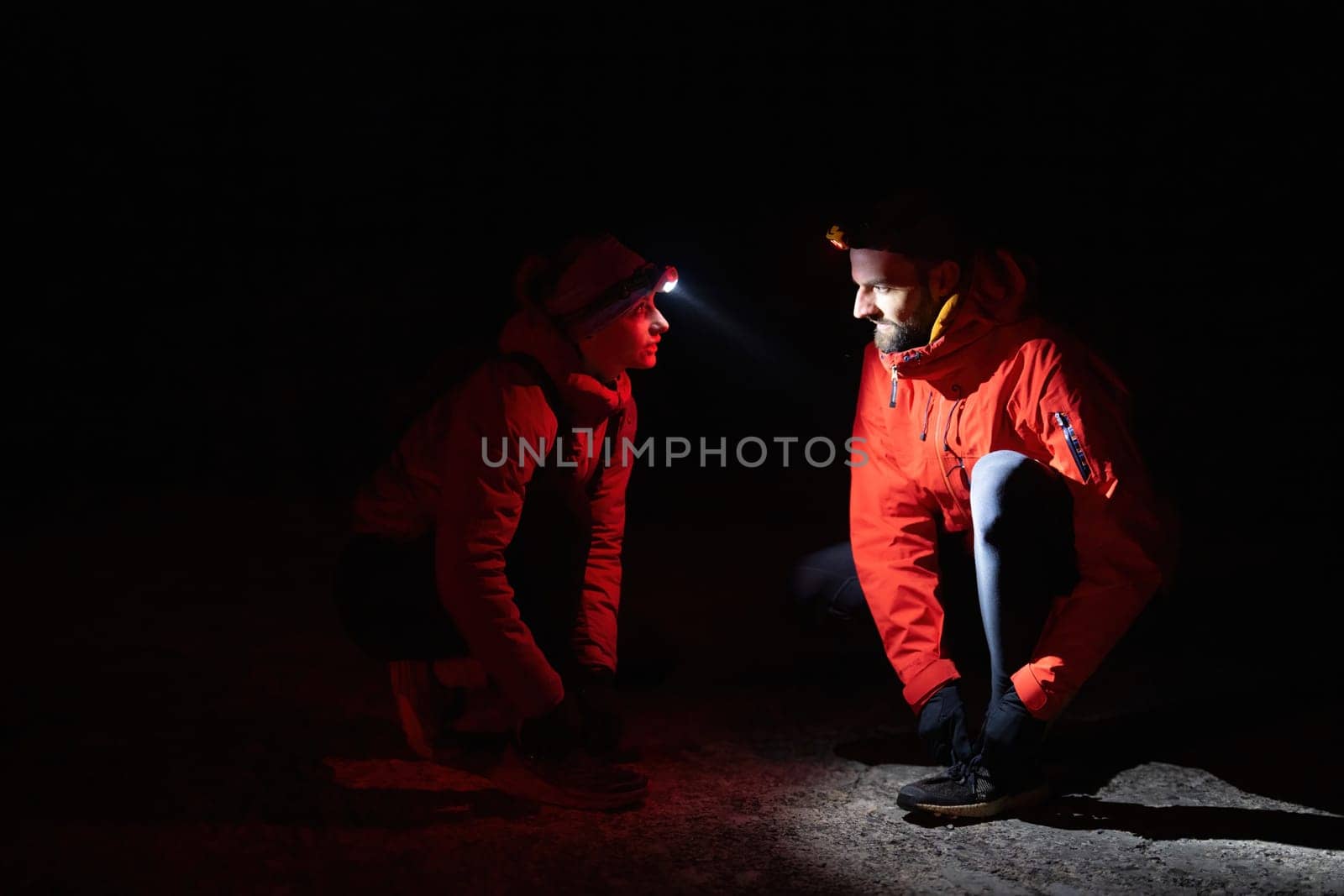 Two trekkers inspect their shoes using headlamps during a night hike, emphasizing safety and preparation in the dark.