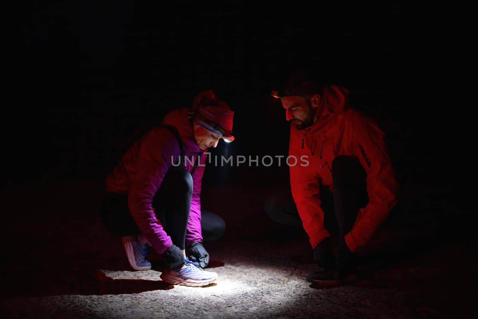 Two trekkers inspect their shoes using headlamps during a night hike, emphasizing safety and preparation in the dark.